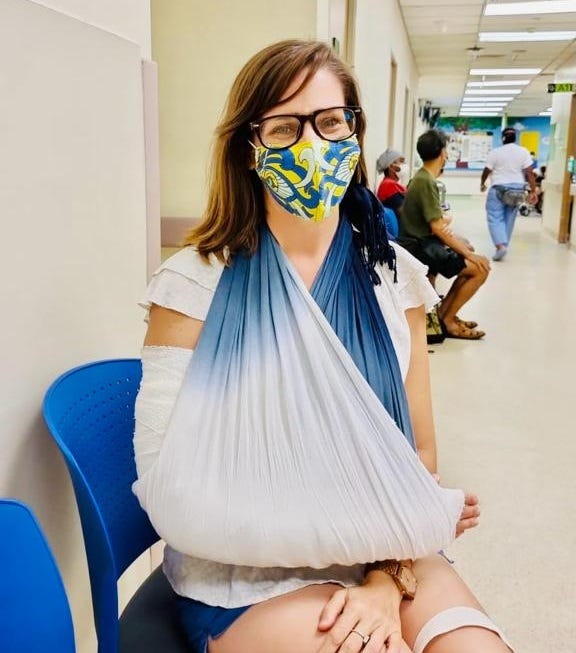 Frau mit Gesichtsmaske und Armschlinge in einem Krankenhaus.