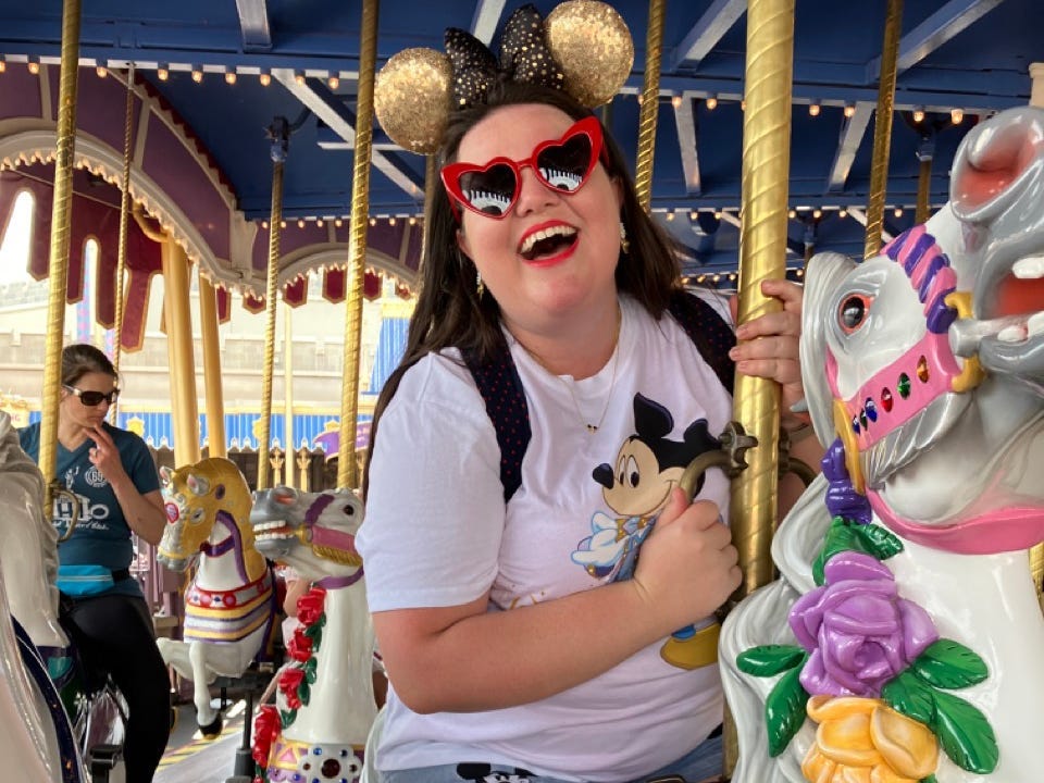 Megan Dubois trägt eine herzförmige Sonnenbrille und lächelnde Minnie-Ohren auf einem Karussell