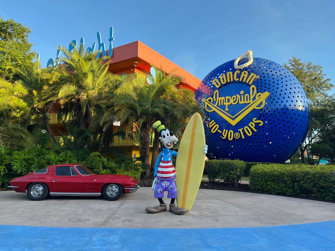 Außenansicht des Disney Pop Century Hotels mit einem großen roten Kunstauto, einem Jo-Jo und einer Goofy-Figur, die ein Surfbrett hält