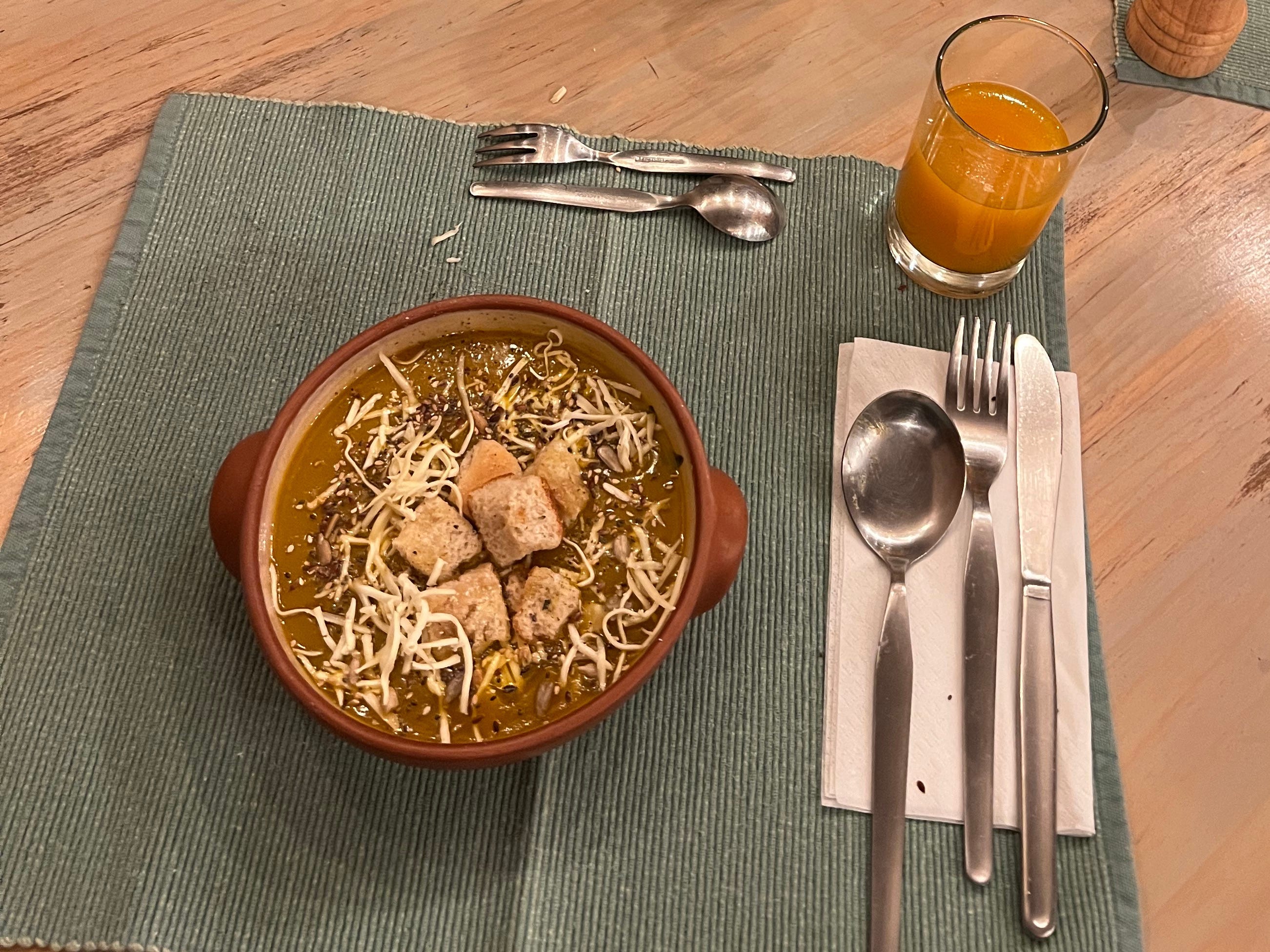 Eine Schüssel Suppe und Besteck auf einem blaugrünen Tischset.