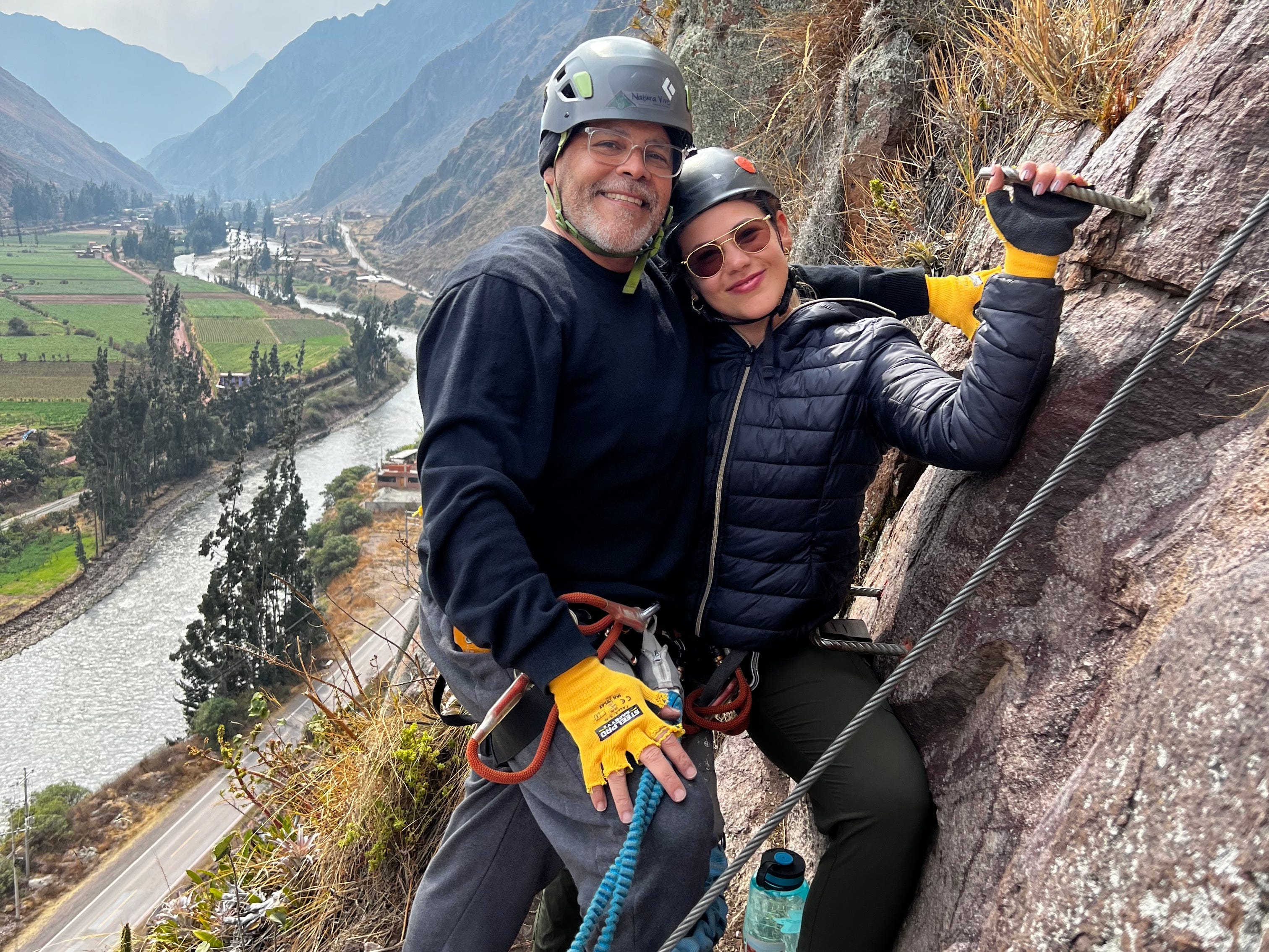 Victoria und ihr Vater lächeln für ein Foto, während sie einen Klettersteig an einer Klippe erklimmen.