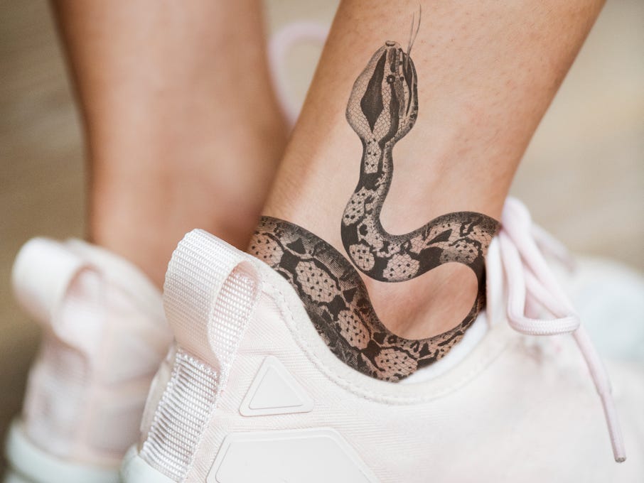 Nahaufnahme des Knöchels einer Person, auf deren Bein ein Schlangen-Tattoo zu sehen ist