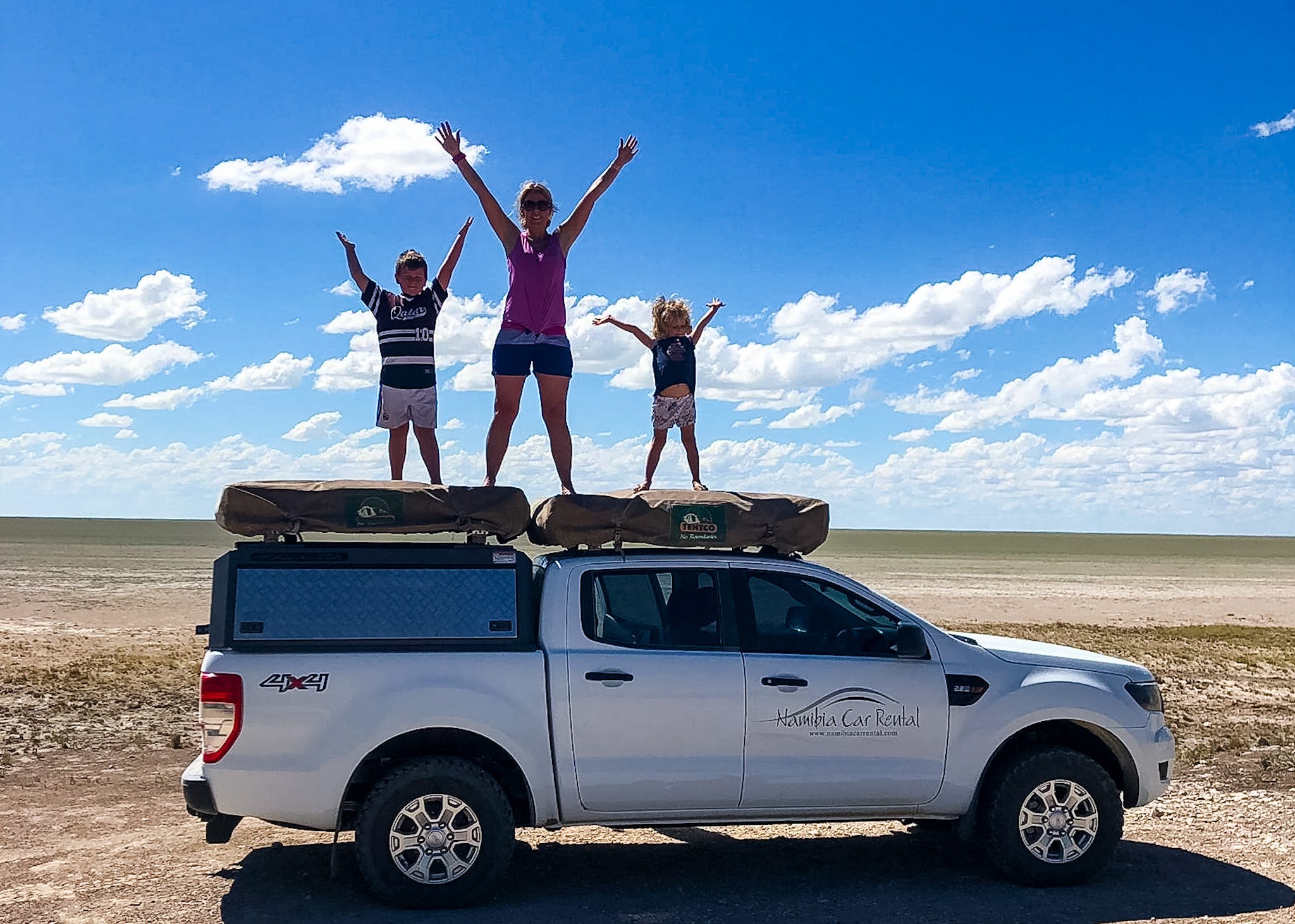 Mutter und zwei Kinder stehen auf dem Dach eines 4x4-Autos in Namibia