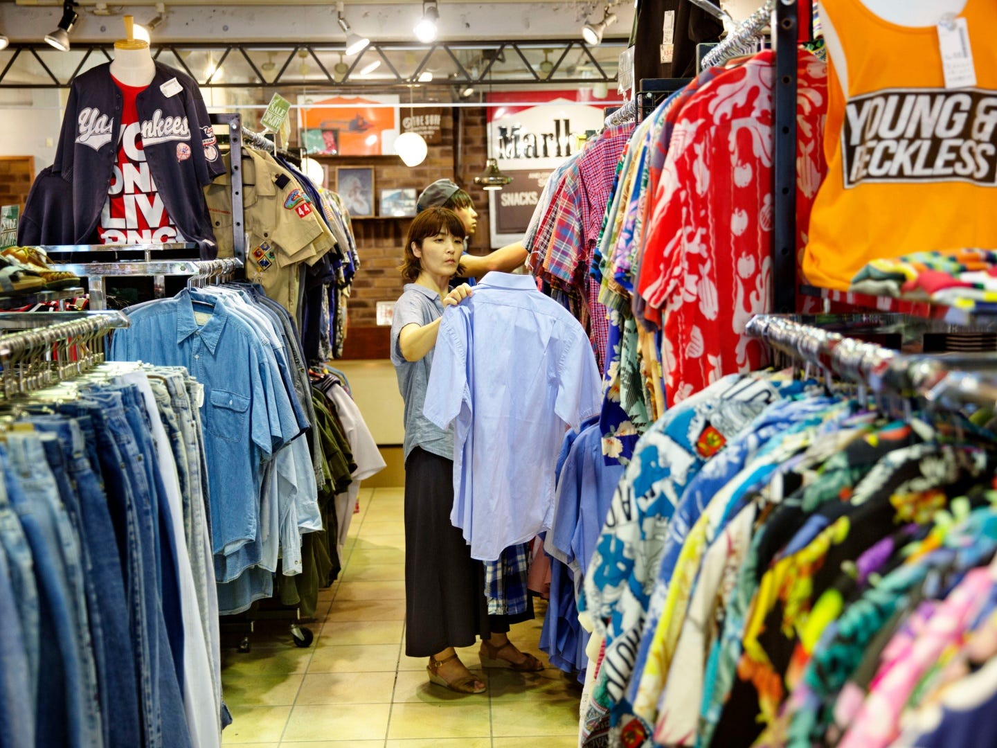 Eine Frau in einem Gebrauchtwarenladen inspiziert ein blaues Kurzarmhemd