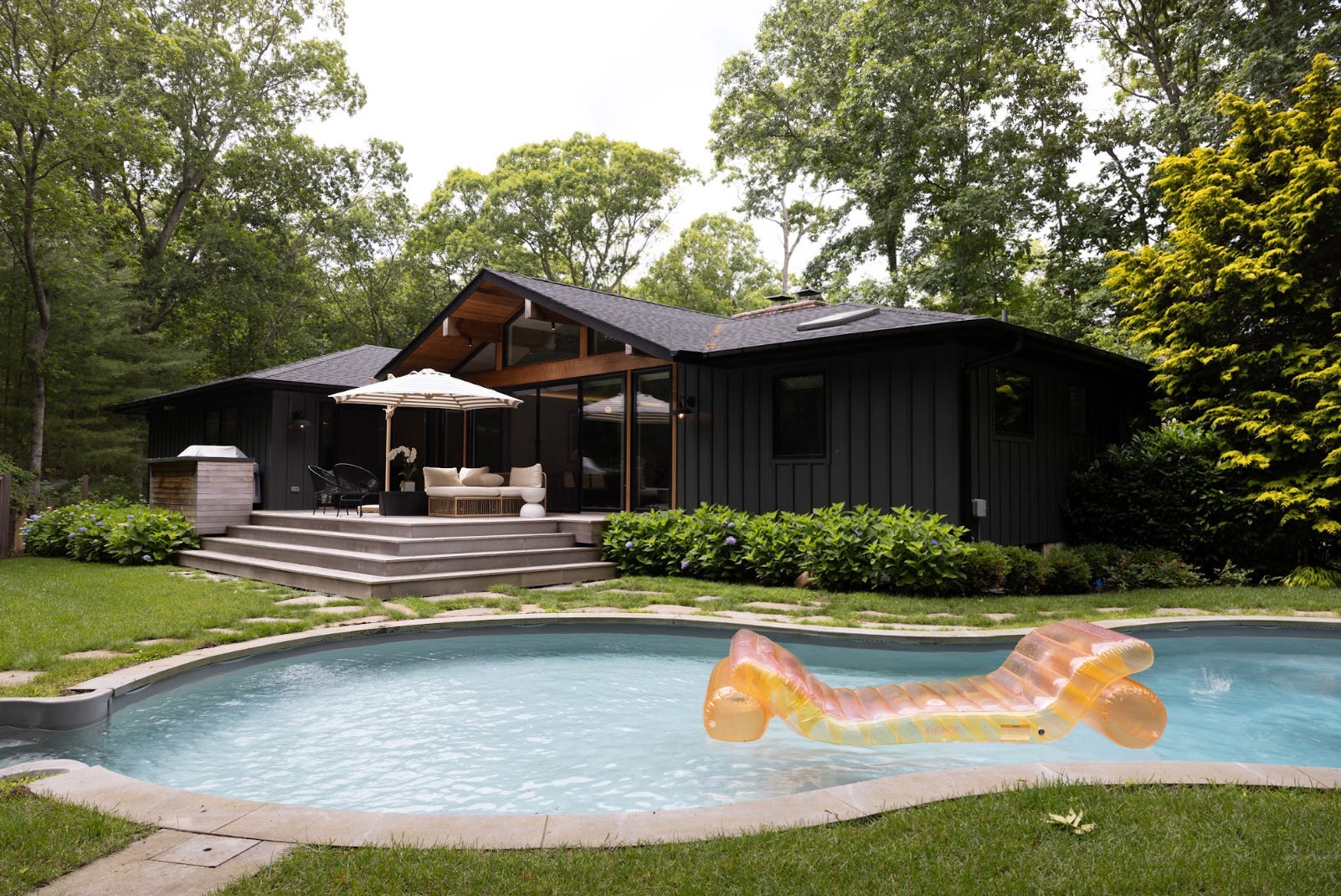 Emilie Gerbers Hampton-Haus mit mattschwarzer Fassade, weitläufigem Garten mit grünem Gras und einem Pool