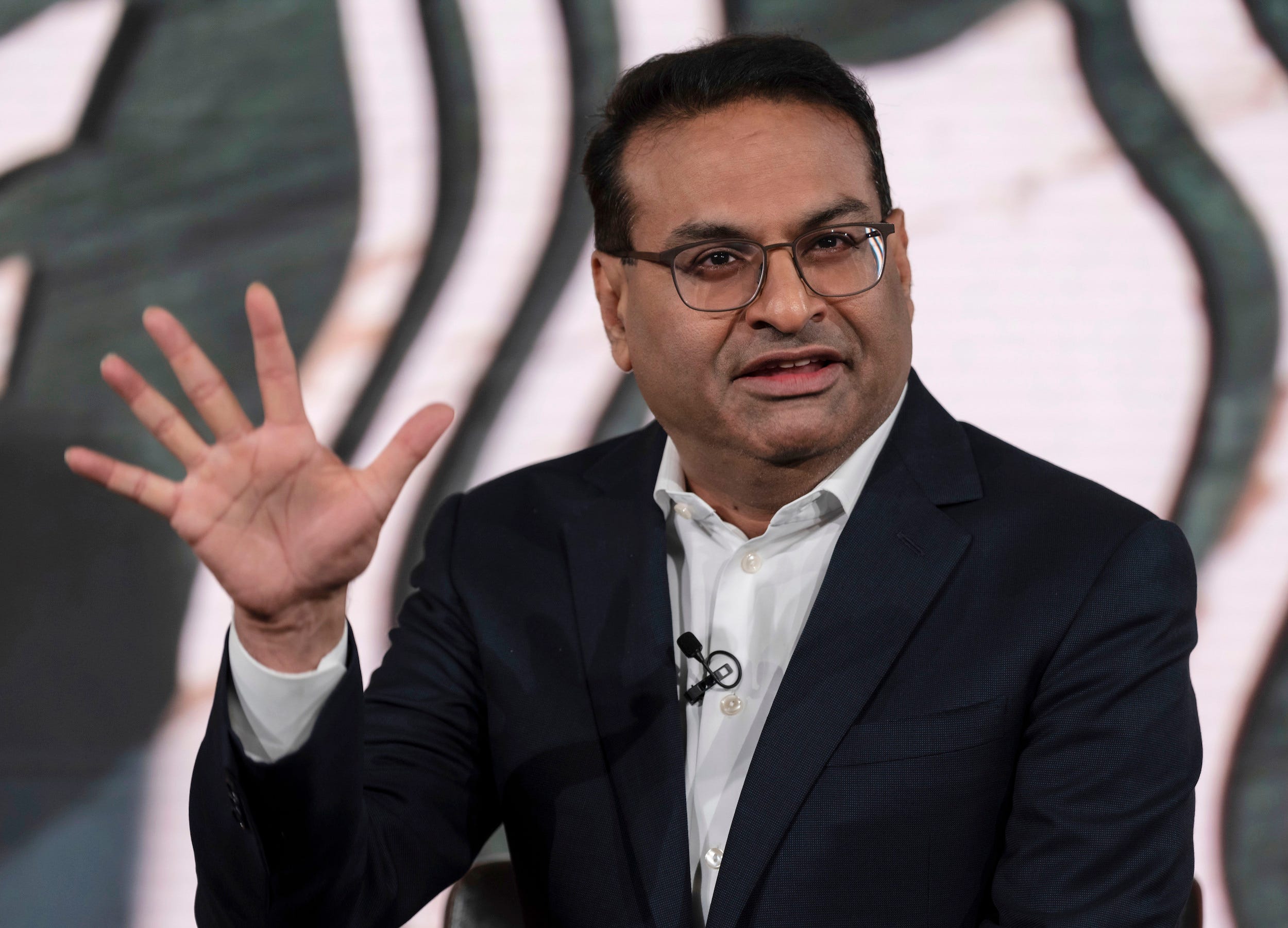 Laxman Narasimhan, der neue CEO von Starbucks, hält die Hand hoch, während er auf der Bühne spricht