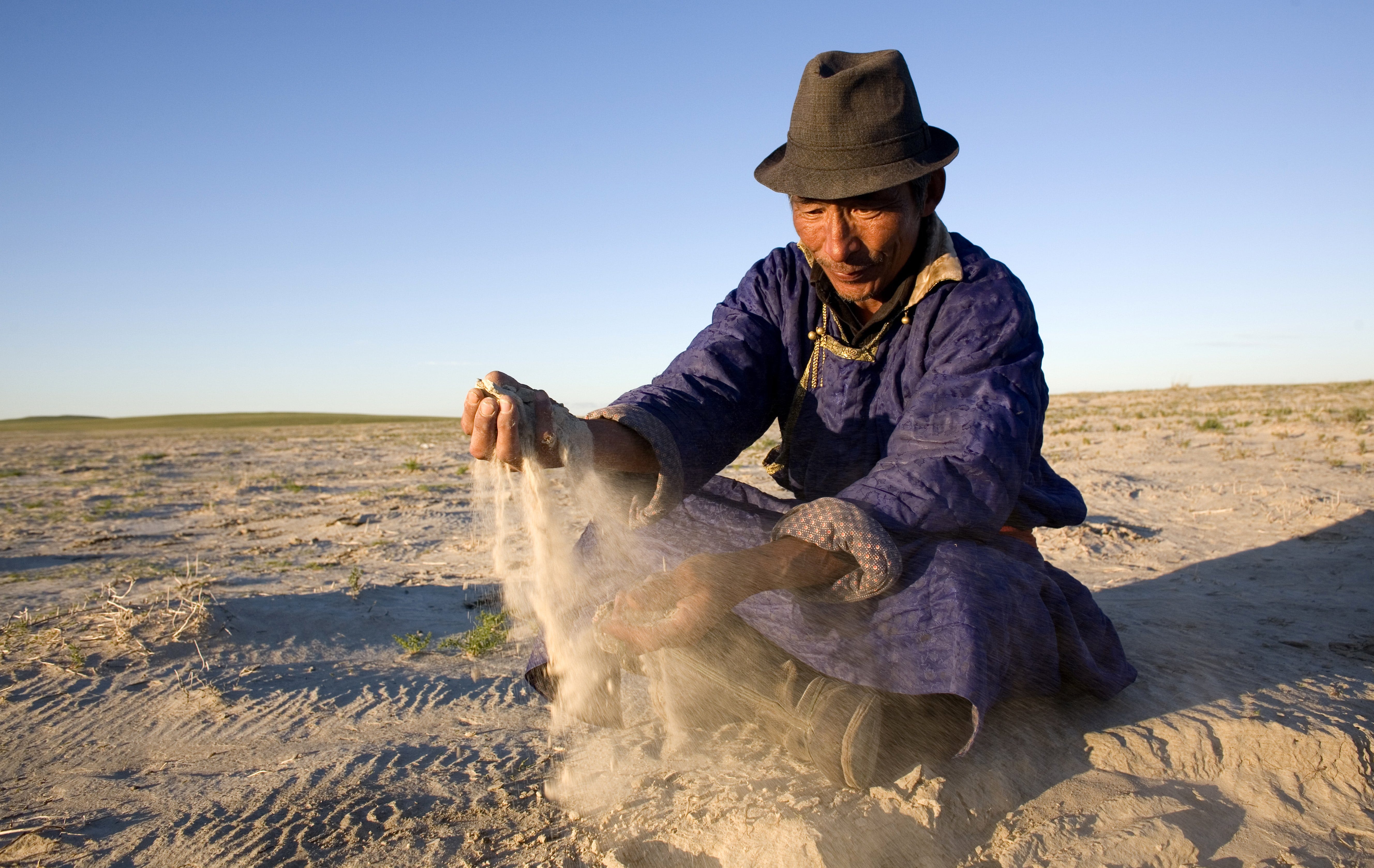 Ein Foto eines mongolischen Nomadenhirten, der Sand aus einem ausgetrockneten Seegrund durch seine Hände laufen lässt.