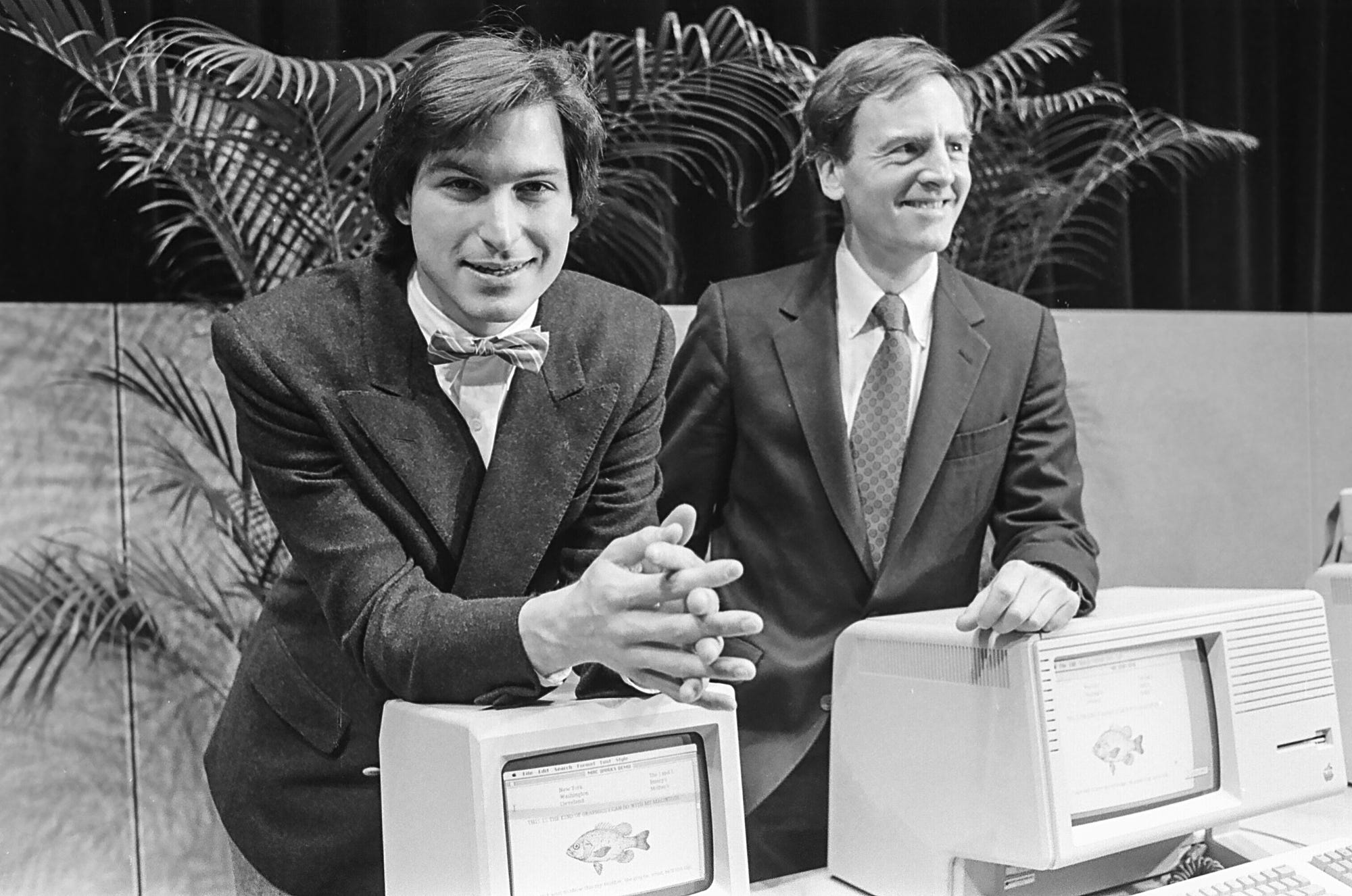 Steve Jobs und John Sculley lehnen sich auf einem Schwarz-Weiß-Foto an Original-Apple-Computer Lisa und Macintosh an