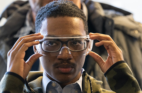 Ein Finalist von JUMP into STEM 2022–2023, der für einen Rundgang durch NREL eine Schutzbrille aufsetzt.