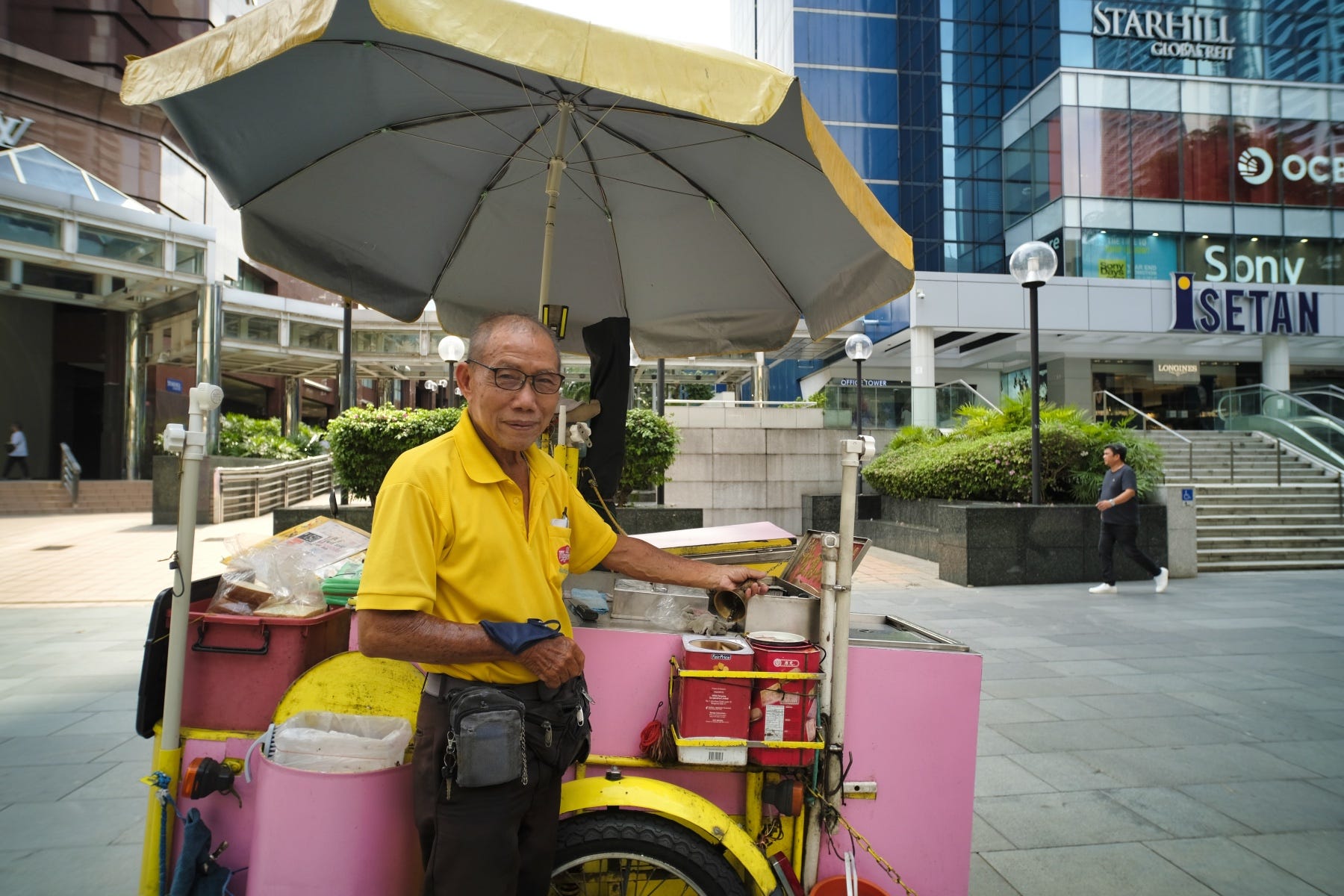 Ein älterer Eisverkäufer posiert neben seinem Eiswagen entlang der Orchard Road.