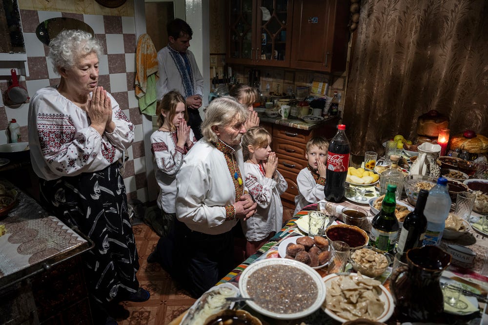Die Familie Selentschuk – zwei ältere Menschen, ein Erwachsener und vier Kinder – betet vor einem mit Essen beladenen Tisch – im Dorf Kryvorivnia, Ukraine, Sonntag, 24. Dezember 2023