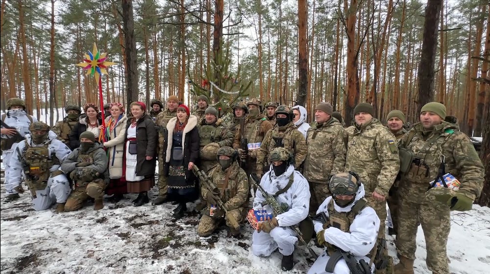 Eine Gruppe ukrainischer Soldaten im Norden der Ukraine steht am 25. Dezember 2023 mit einer Gruppe von Sängern in einem verschneiten Wald.