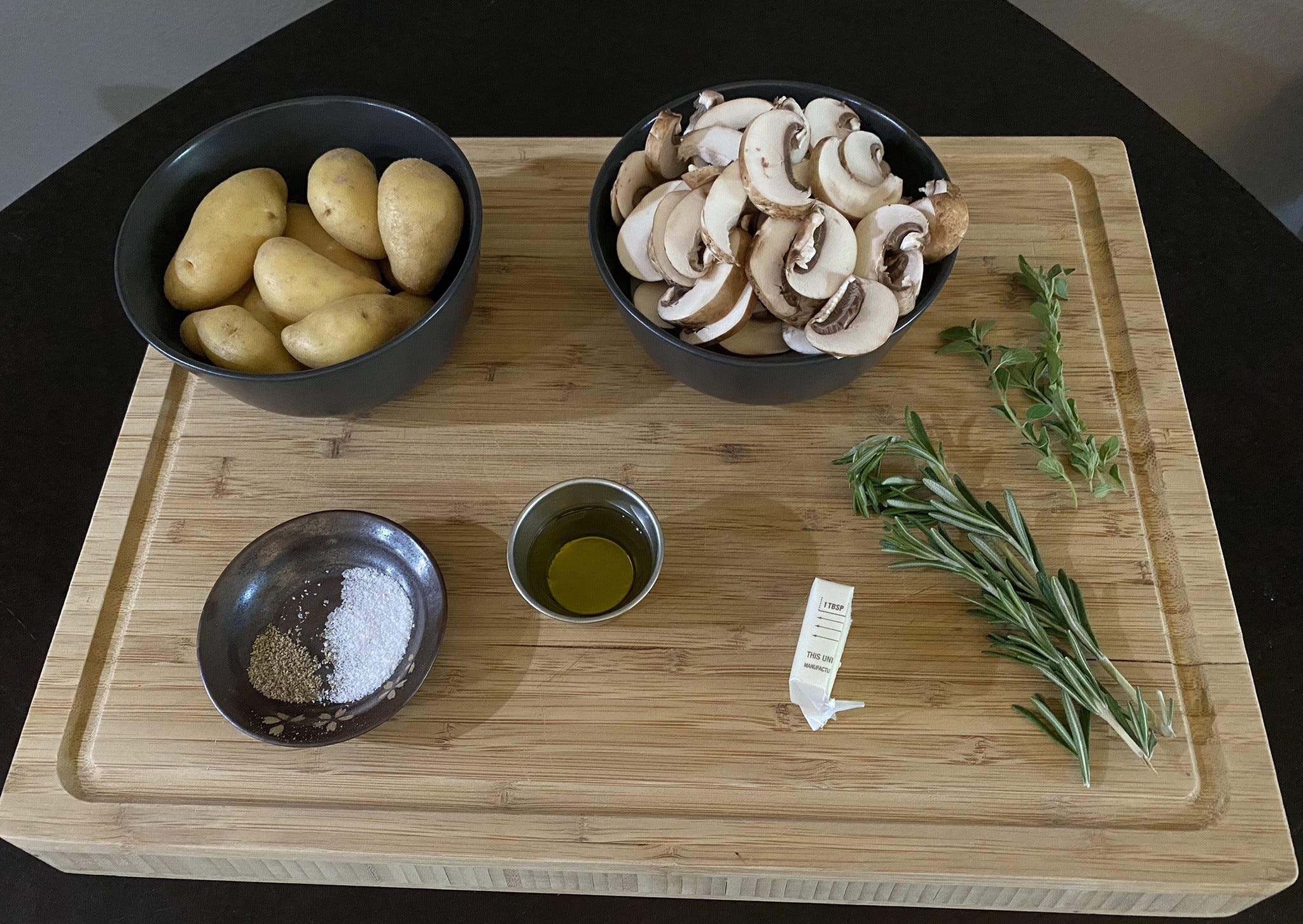 Kartoffeln, Pilze, Gewürze, Öl, Butter und Kräuter auf einem Holzschneidebrett