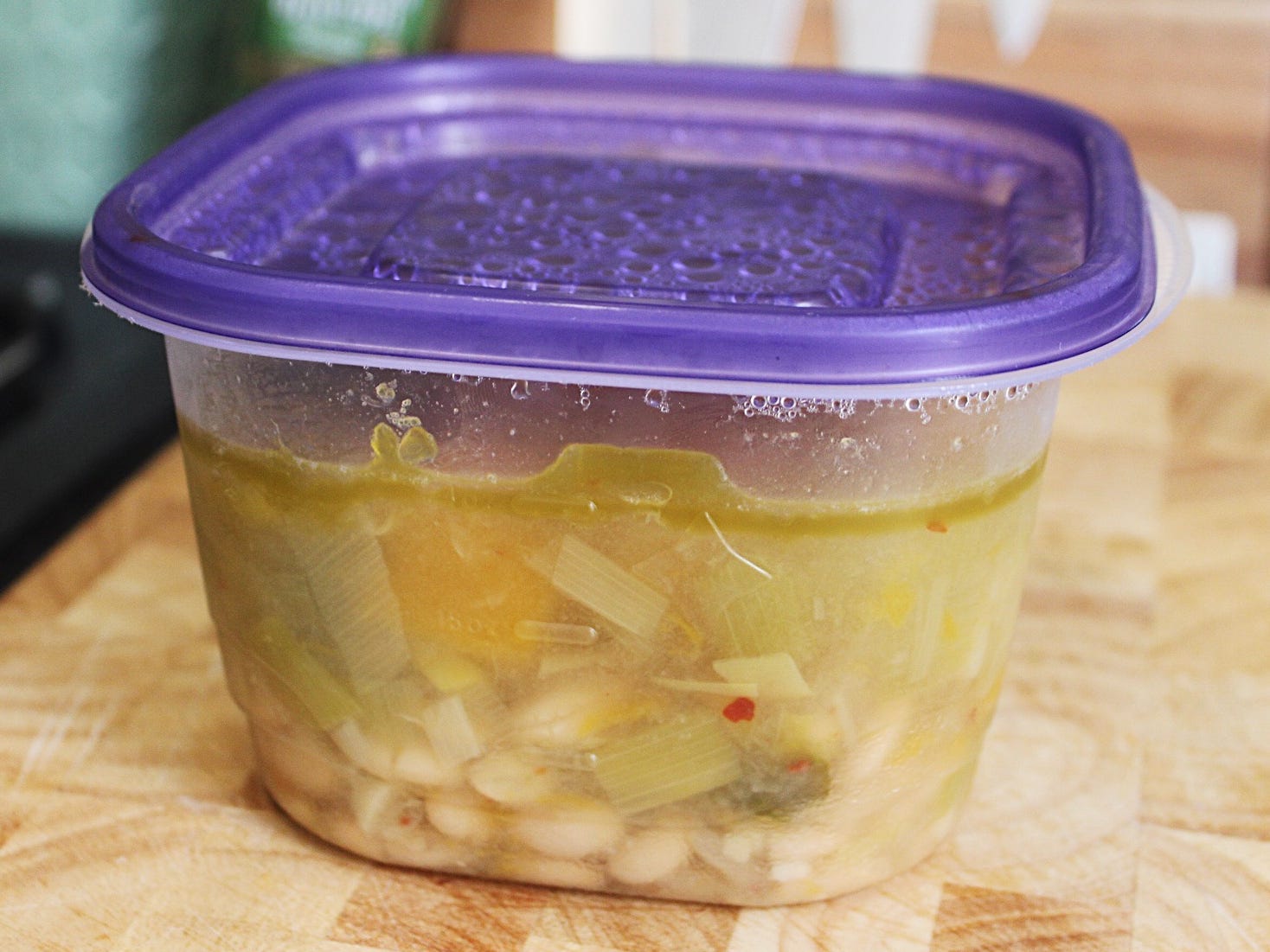 Weiße Bohnensuppe in einem Tupperware-Behälter mit violettem Deckel
