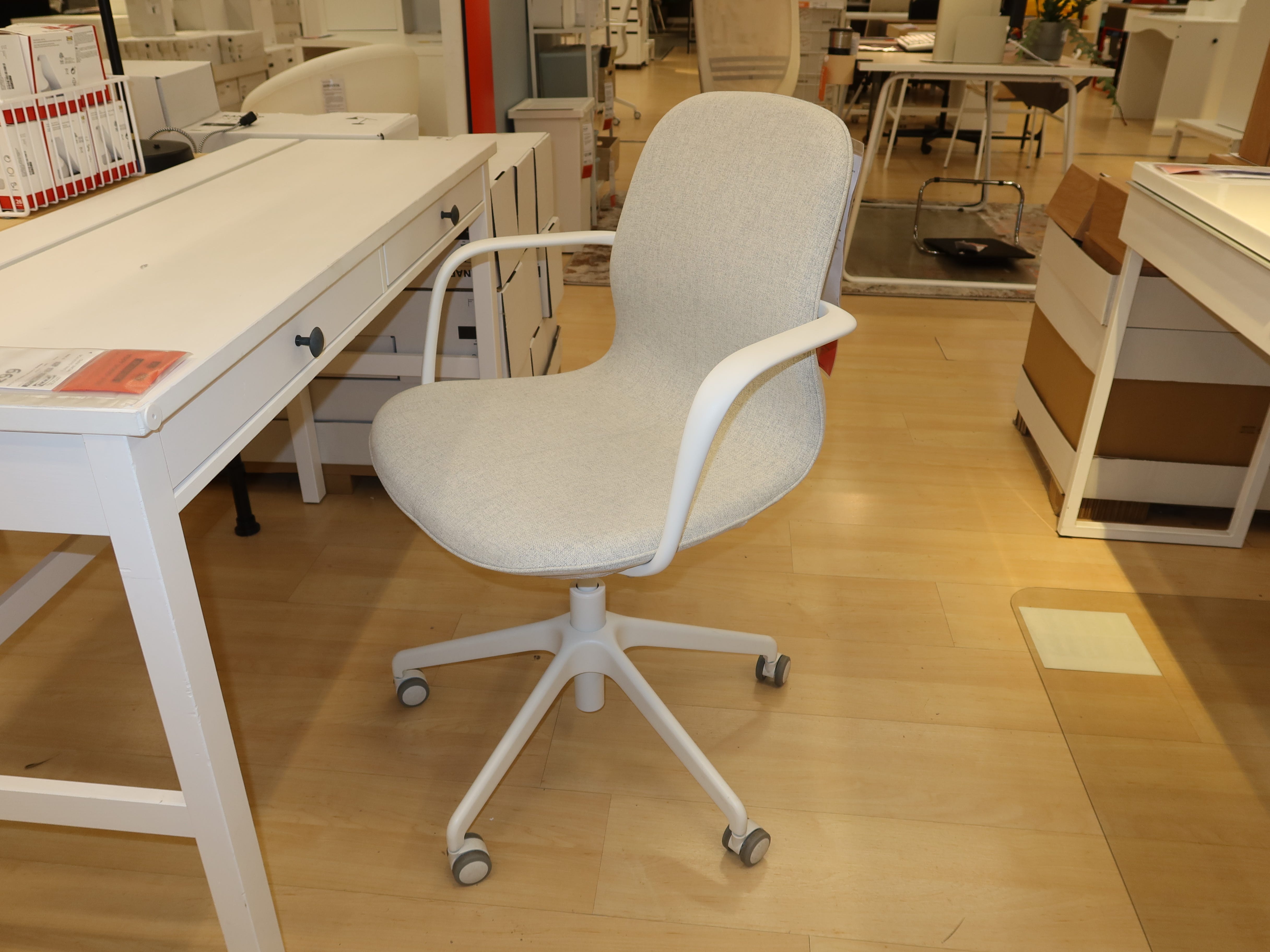 Grauer Bürostuhl mit weißen Metalldetails vor einem weißen Schreibtisch und einem Holzboden