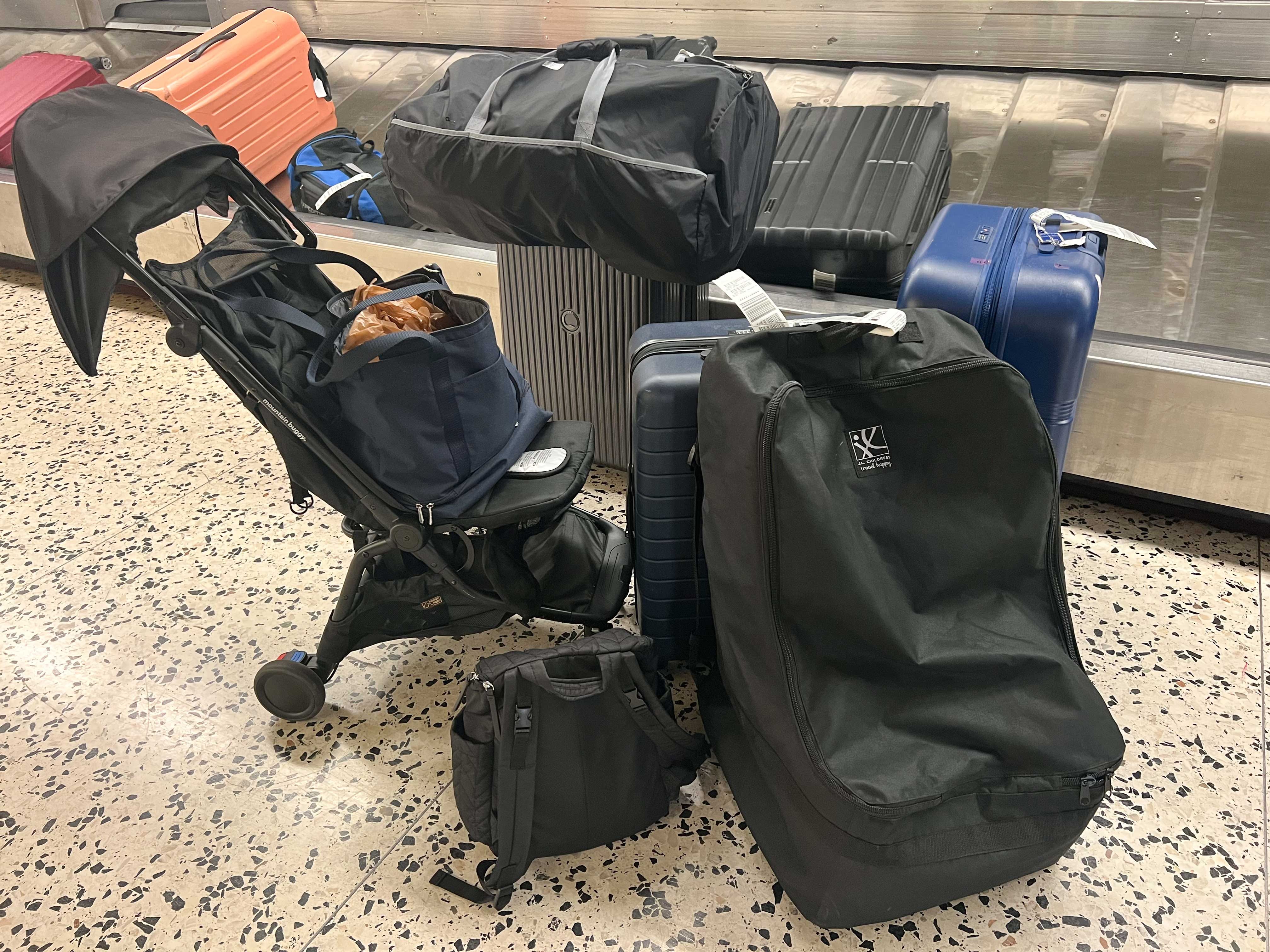 Mehrere große Gepäckstücke, ein Kinderwagen und kleinere Taschen stehen neben einem Gepäckband an einem Flughafen.