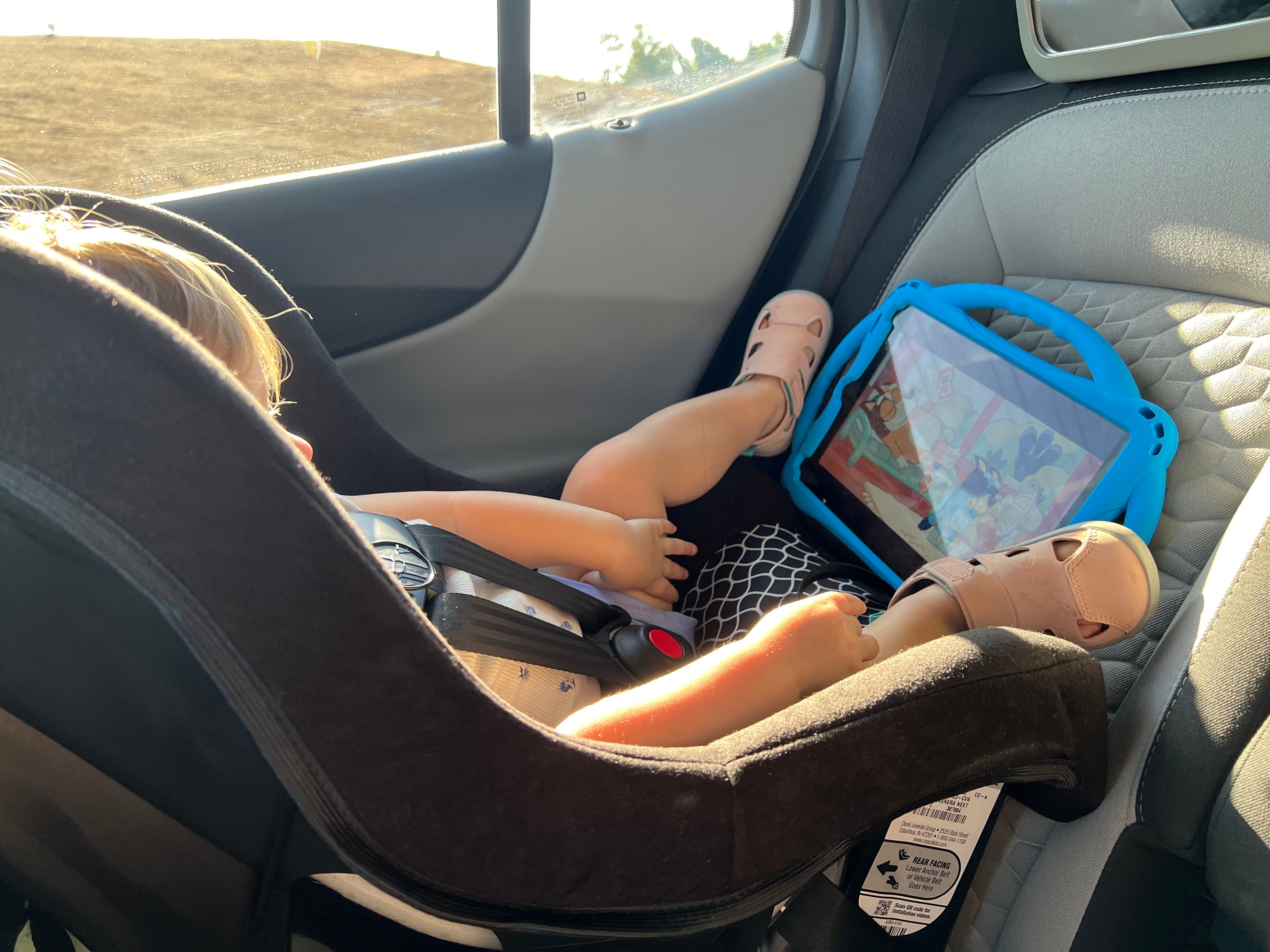 Ein Kind sitzt in einem Autositz und schaut auf ein blaues iPad.