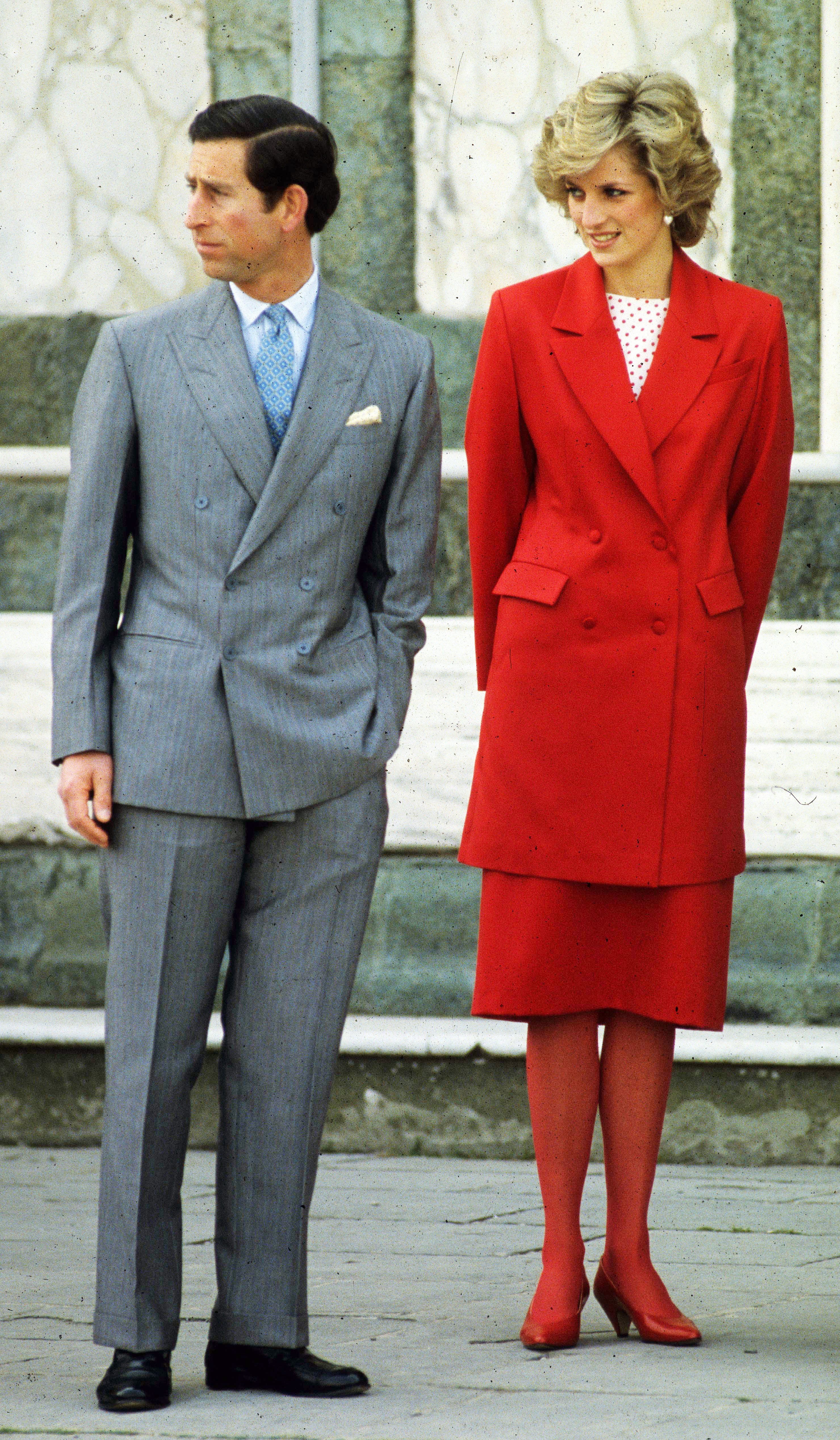 Prinzessin Diana mit Prinz Charles in Florenz.  Er trägt ein.  Sie trägt einen grauen Herrenanzug, eine lange rote Jacke, einen roten Rock, rote Strumpfhosen und rote Schuhe, dazu ein rot-weiß gepunktetes Oberteil.