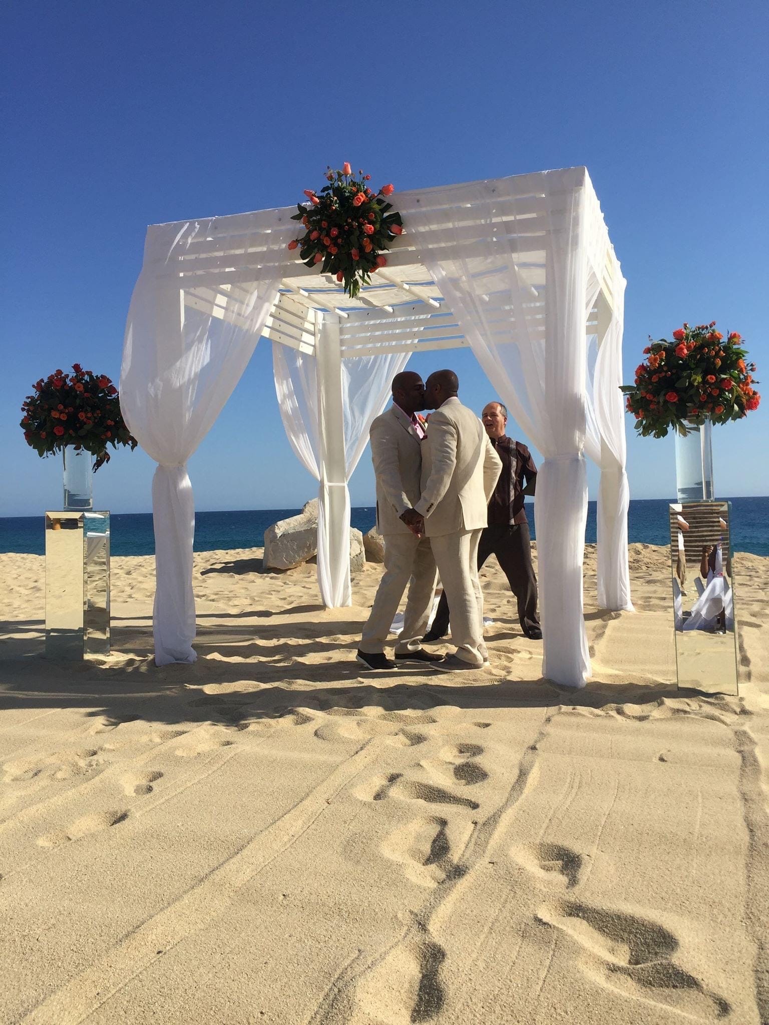 Paar küsst sich unter einer Pergola am Strand und heiratet