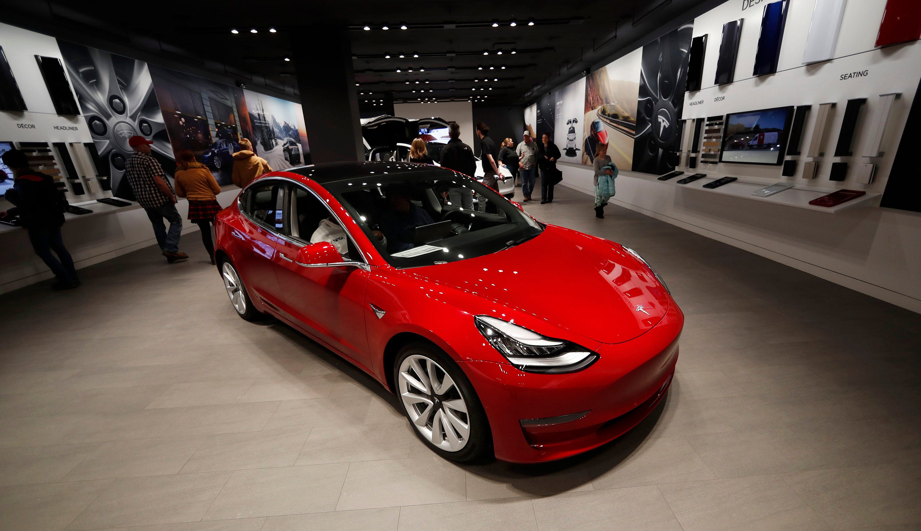 Ein roter Tesla Model 3 auf dem Boden eines Ausstellungsraums.