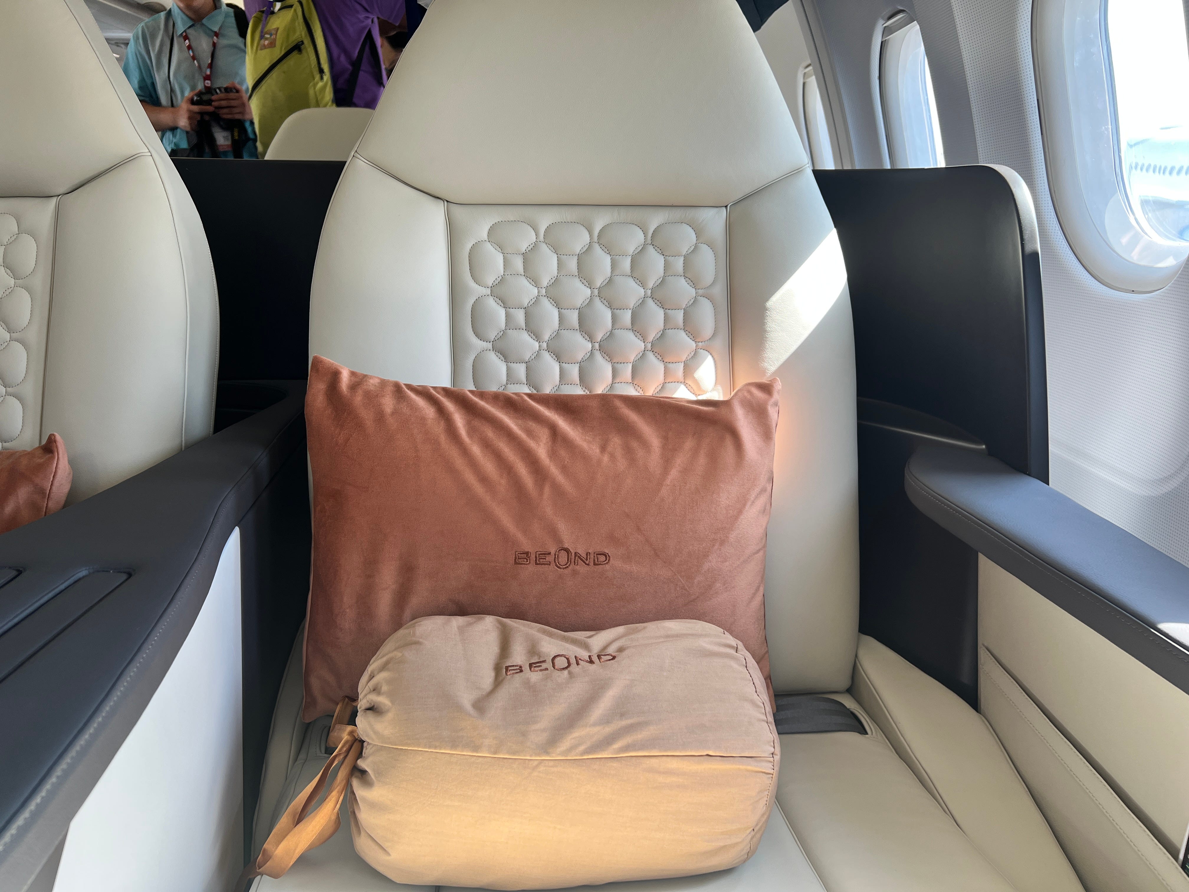 Eine Nahaufnahme des orangefarbenen Kissens und einer Tasche mit Beond-Logo auf einem cremefarbenen Sitz des A319