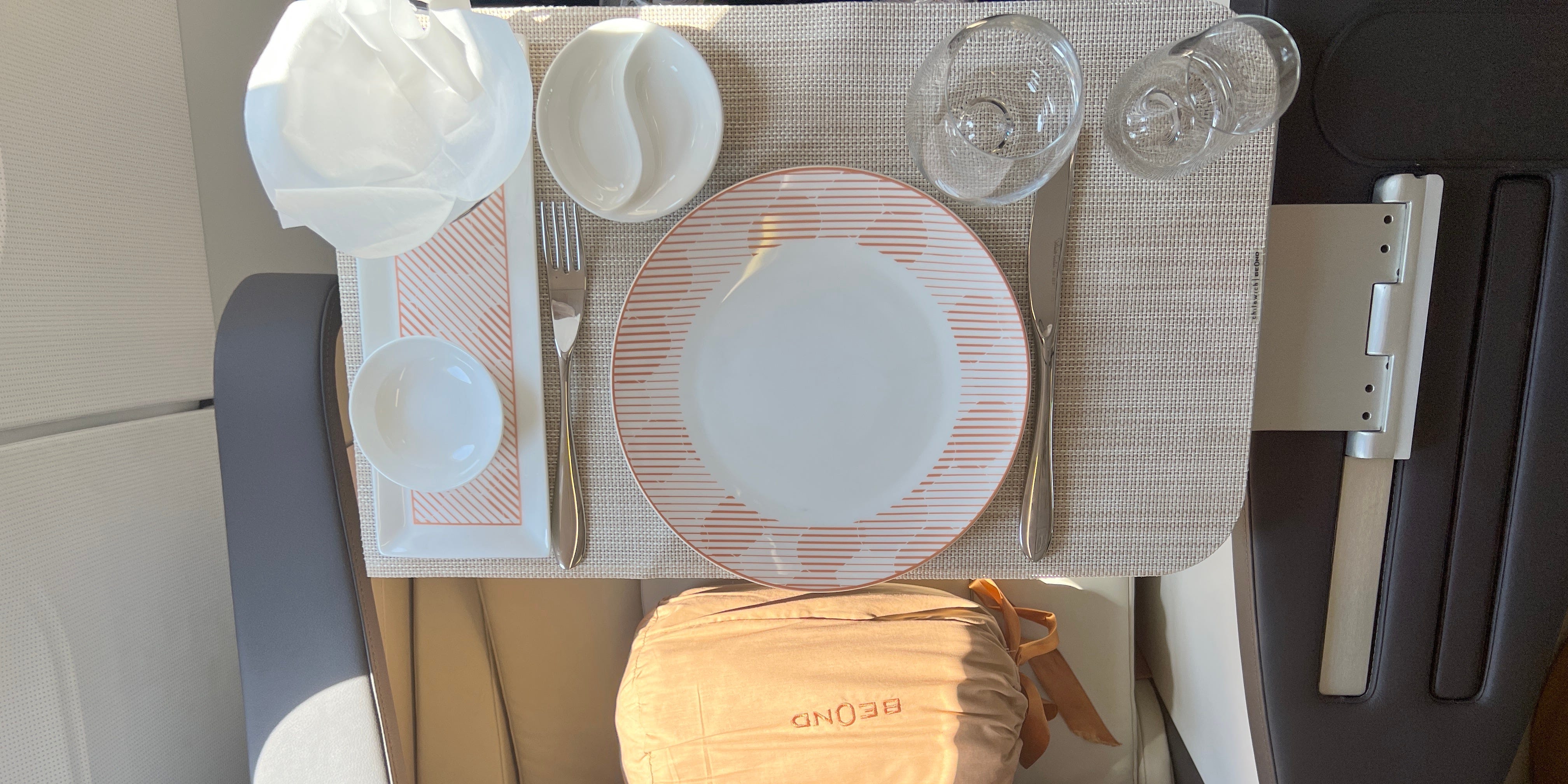 Eine Aufnahme des Abendessens an Bord der Beond A319 von oben nach unten, mit weißem Geschirr mit orangefarbenen Akzenten, zwei Gläsern und ein paar Töpfen