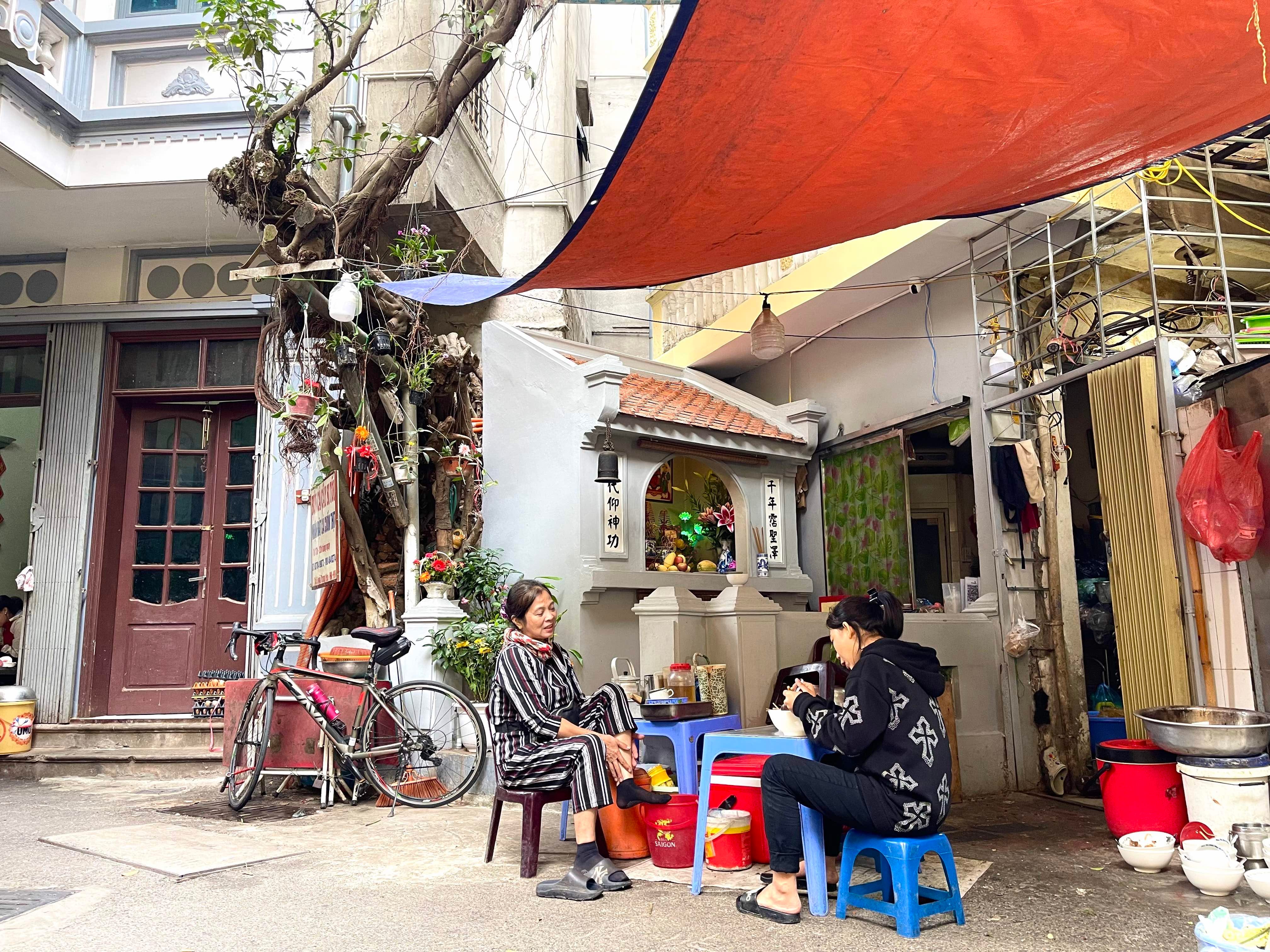 Zwei Frauen sitzen auf blauen Stühlen in einem Nudelladen in Hanoi