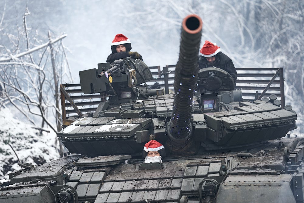Drei Soldaten mit Weihnachtsmützen bemannen am 24. Dezember 2023 einen in Weihnachtslichter gehüllten T-64-Kampfpanzer vor verschneitem Hintergrund.