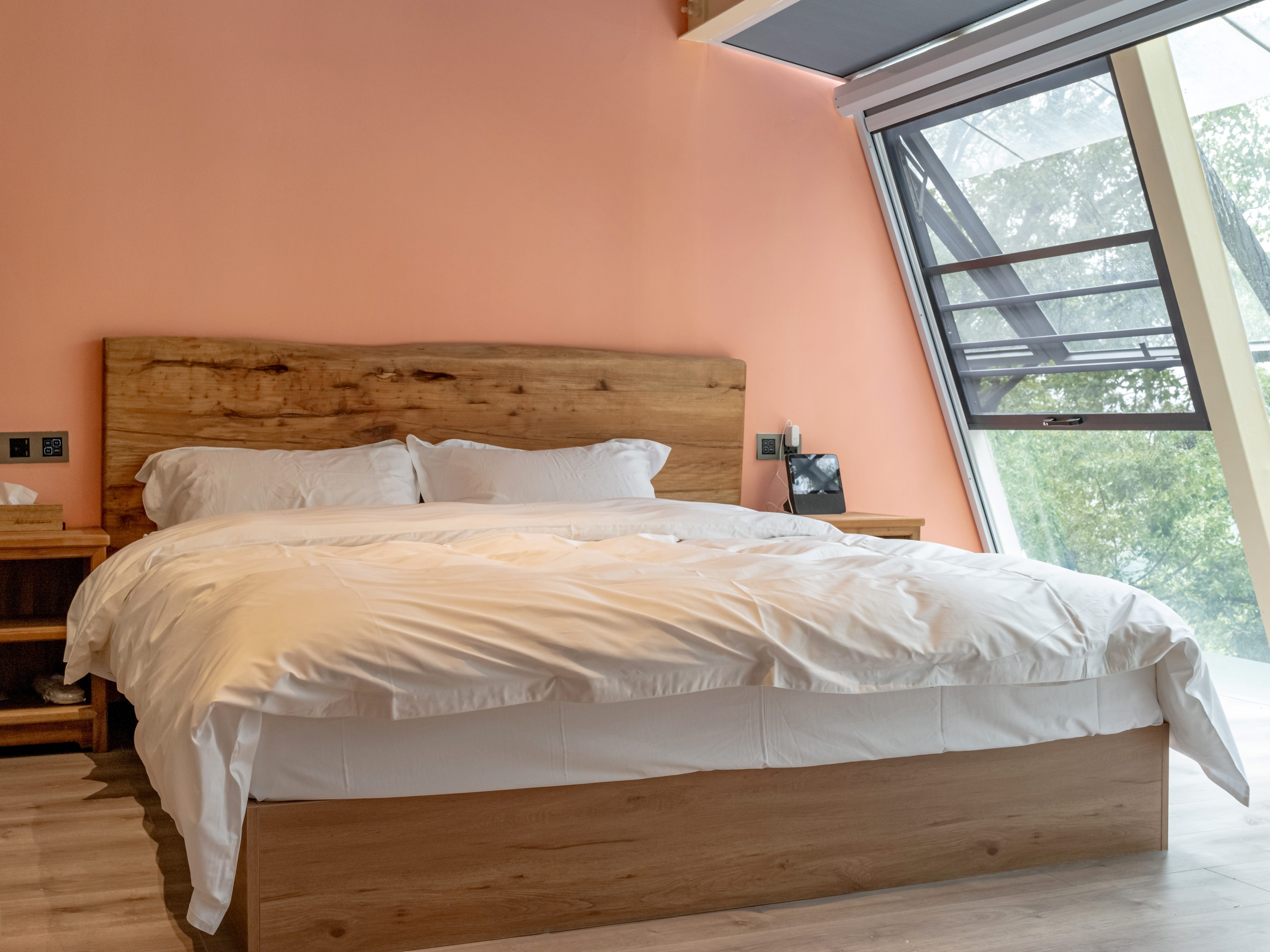 Ein Schlafzimmer mit Korallenwänden, einem raumhohen Fenster und einem Bett mit integriertem Kopfteil aus Holz.