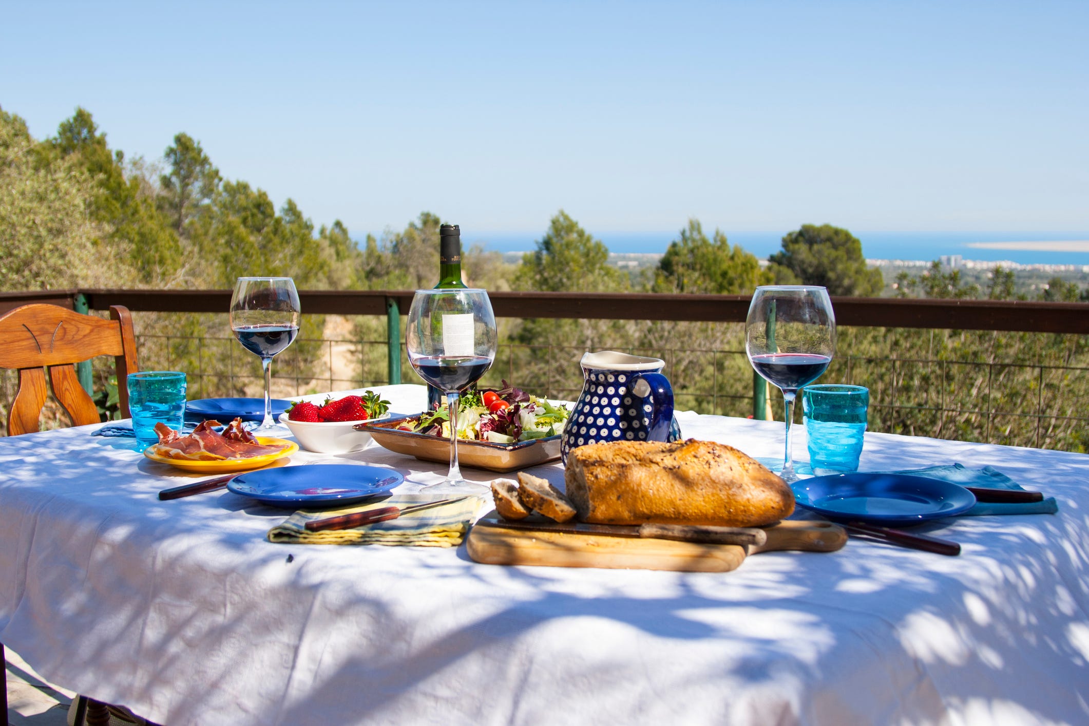 Ein Tisch mit Blick auf das Meer, darauf ein Laib Brot, ein großer Salat und mehrere Gläser Wein.