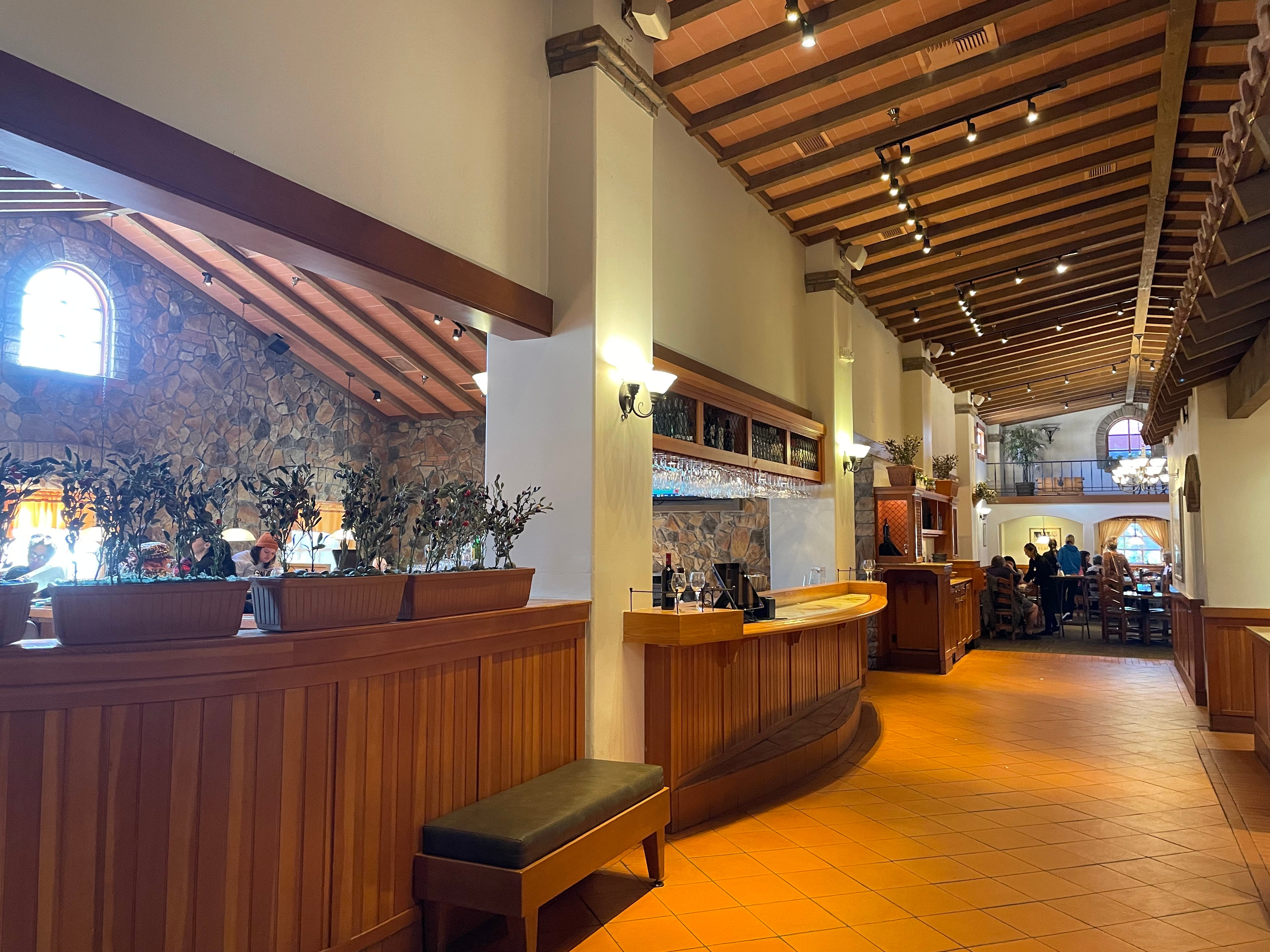Innenflur im Olive Garden mit Holzvertäfelung und -decke, hellbraunem Fliesenboden und Pflanzen an der Wand