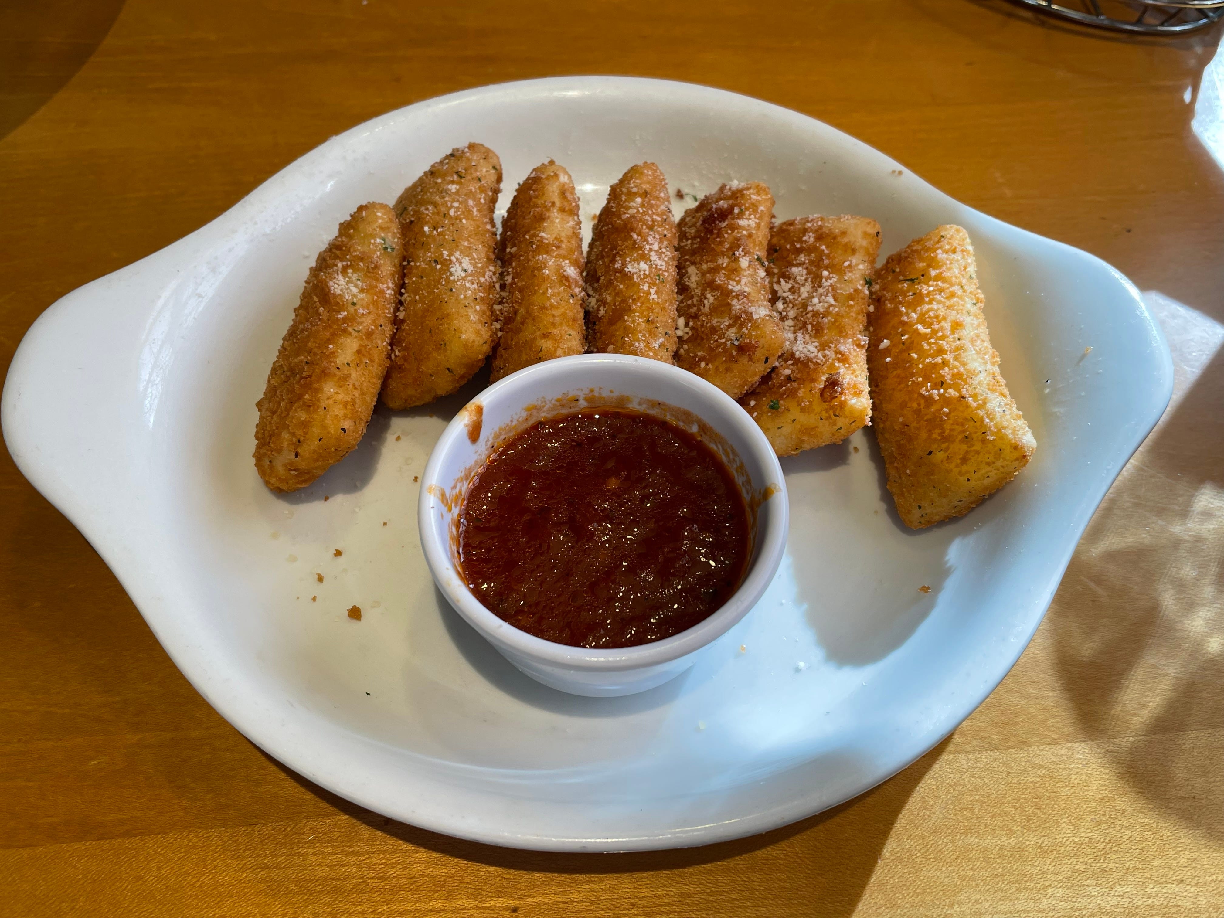 Weißer Teller mit rechteckigen Mozzarella-Sticks mit Marinara-Sauce auf einem braunen Tisch im Olive Garden