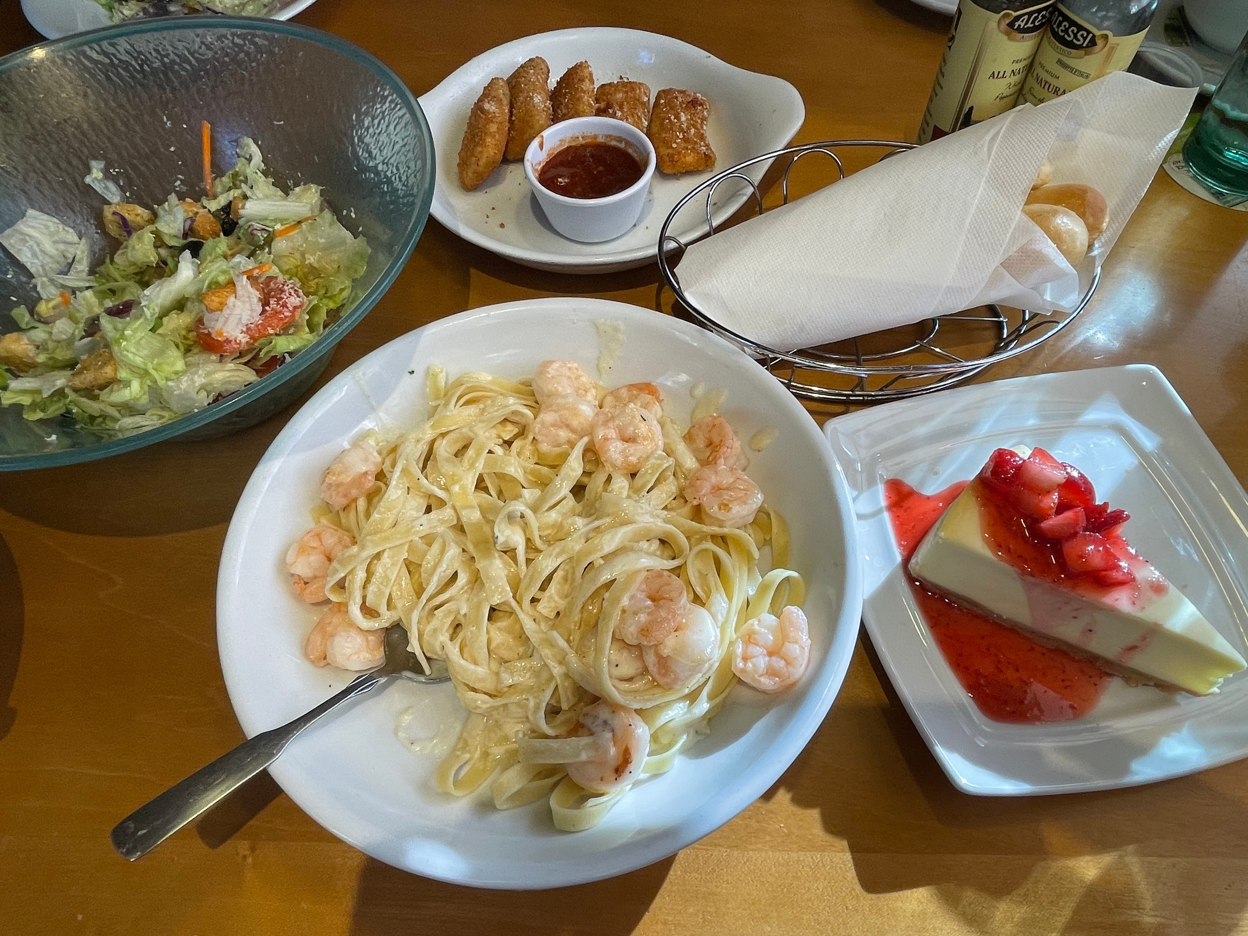 Tisch voller Alfredo-Garnelen, Erdbeer-Käsekuchen, Mozzarella-Sticks, Grissini und Salat im Olive Garden