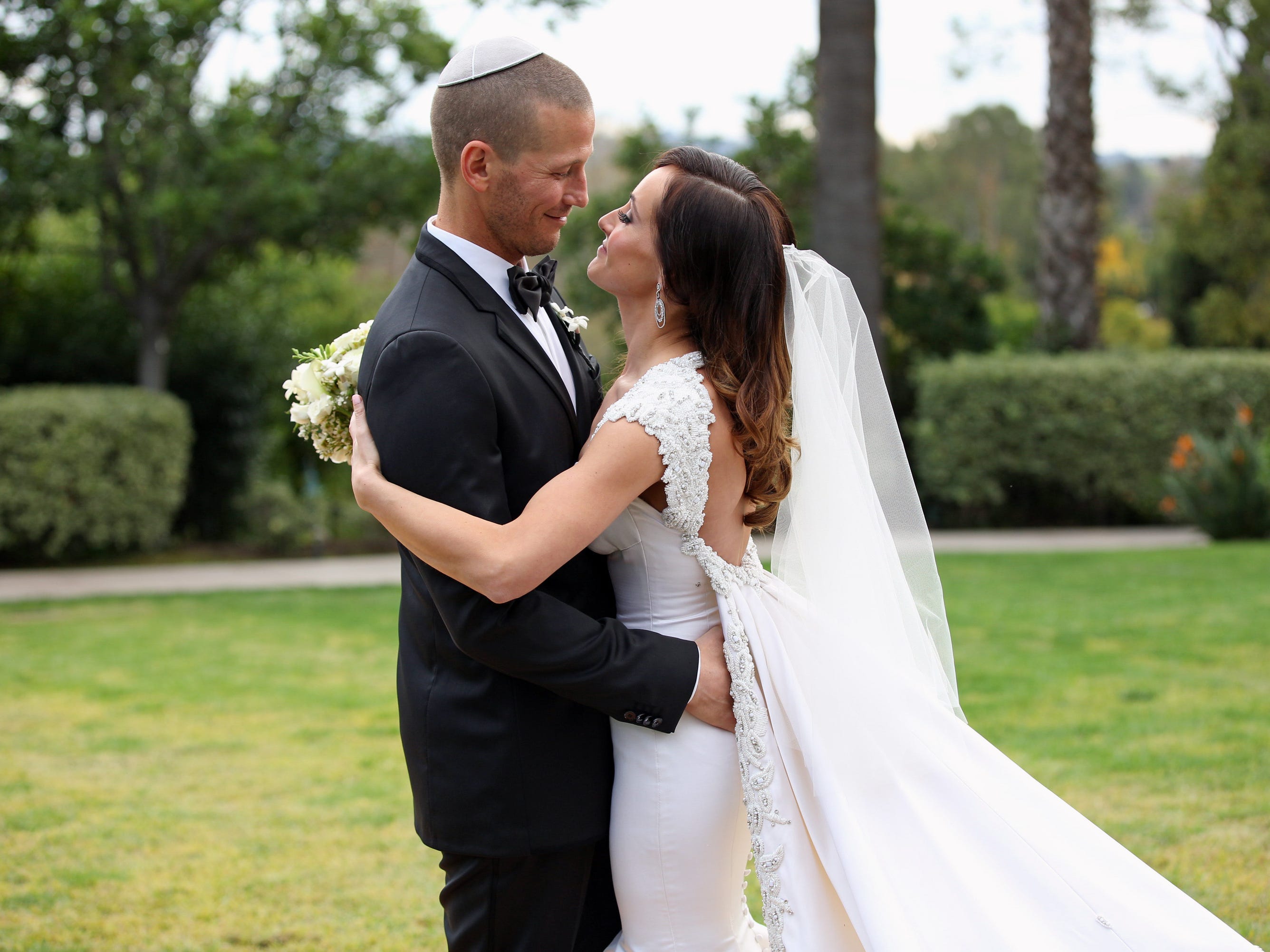 JP Rosenbaum umarmt Ashley Hebert in einem weißen rückenfreien Hochzeitskleid und Schleier an ihrem Hochzeitstag im Jahr 2012 in einem Smoking und einer weißen Yarmulke.
