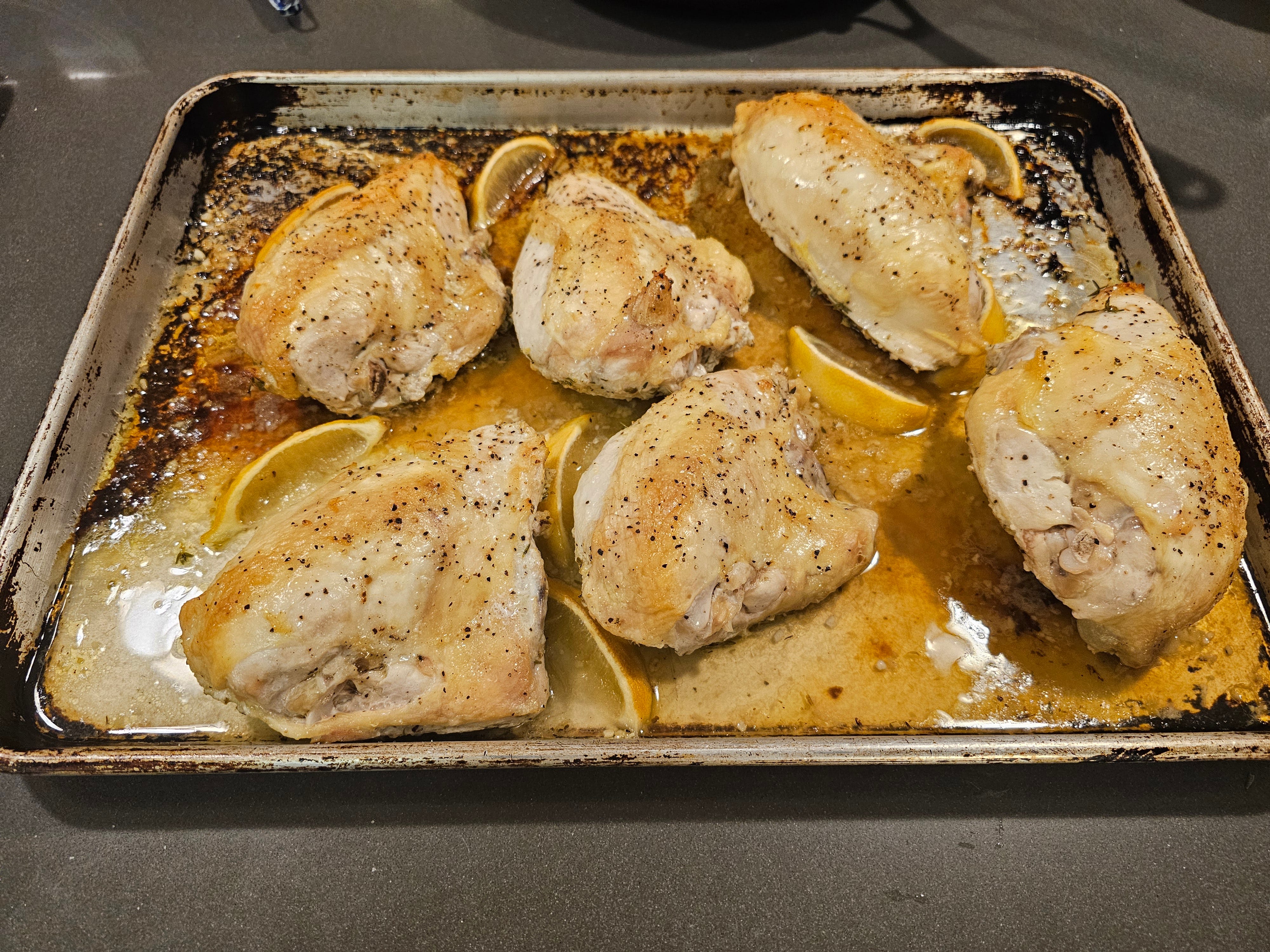 Kochblatt mit gekochten Hähnchenstücken mit Säften und Zitronenschnitzen