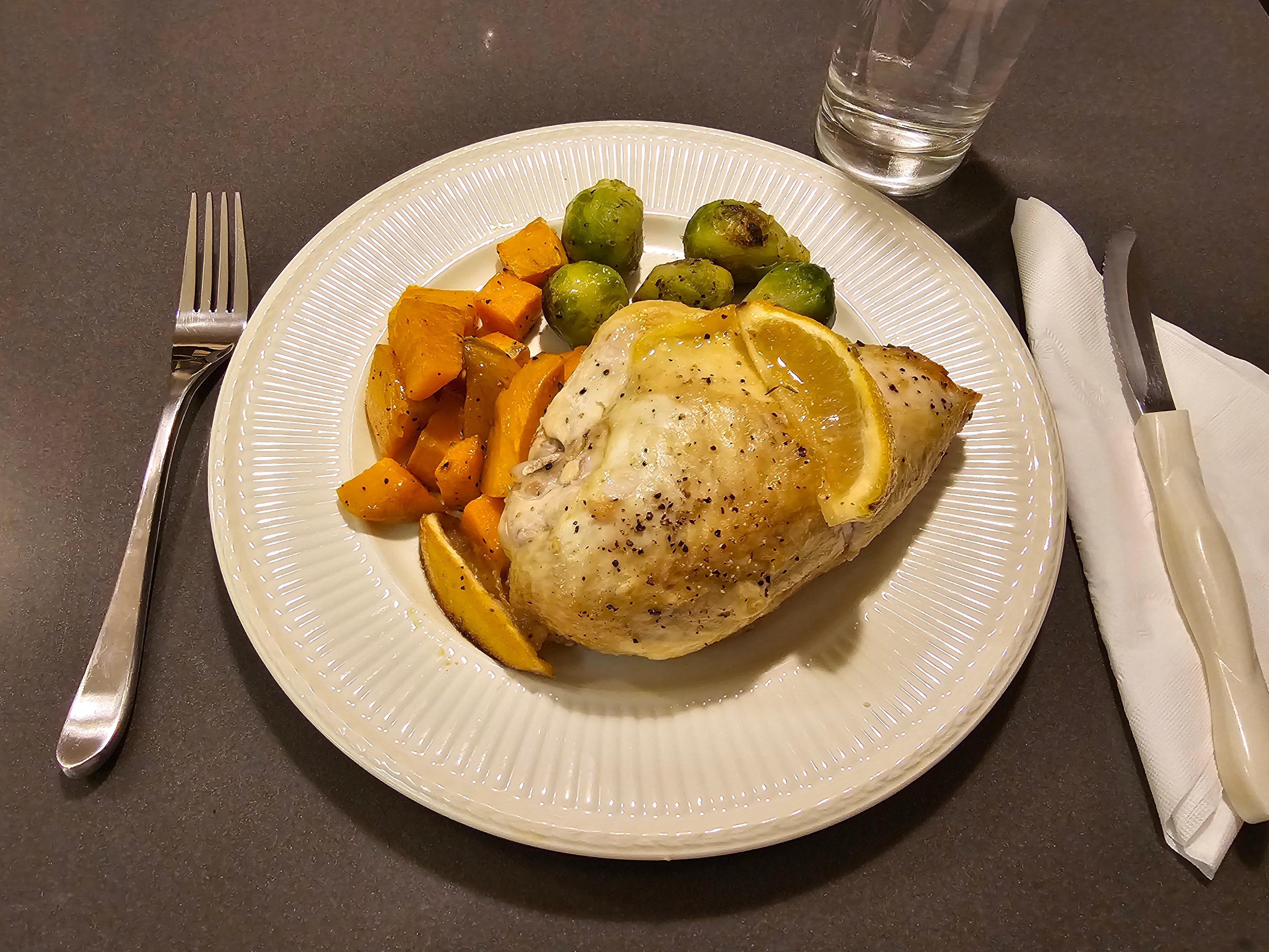Lemno-Hähnchen auf einem Teller mit Rosenkohl und Süßkartoffelwürfeln und einer Zitronenscheibe