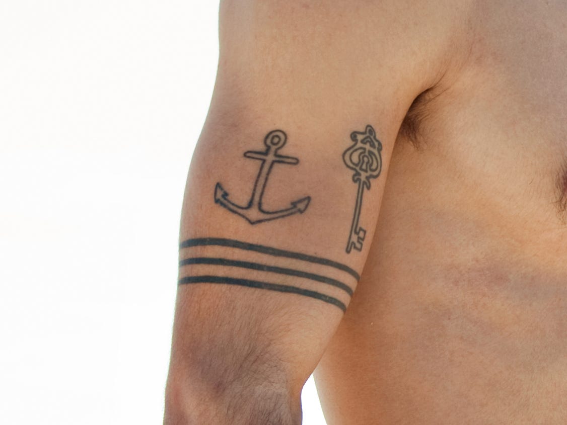 Surfer-Typ mit Ankerschlüssel und Drei-Band-Tattoo, der vom Strand aus auf das Meer blickt