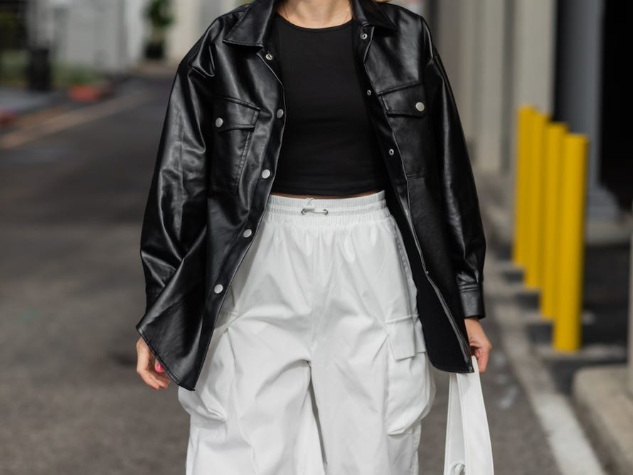 Frau geht eine Straße entlang und trägt eine schwarze Lederjacke über einem schwarzen T-Shirt und einer weißen Cargohose mit weitem Bein