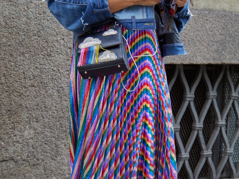 Person, die auf einem Bürgersteig auf ihr Telefon schaut und eine Jeansjacke und einen regenbogenfarbenen, metallischen Faltenrock trägt