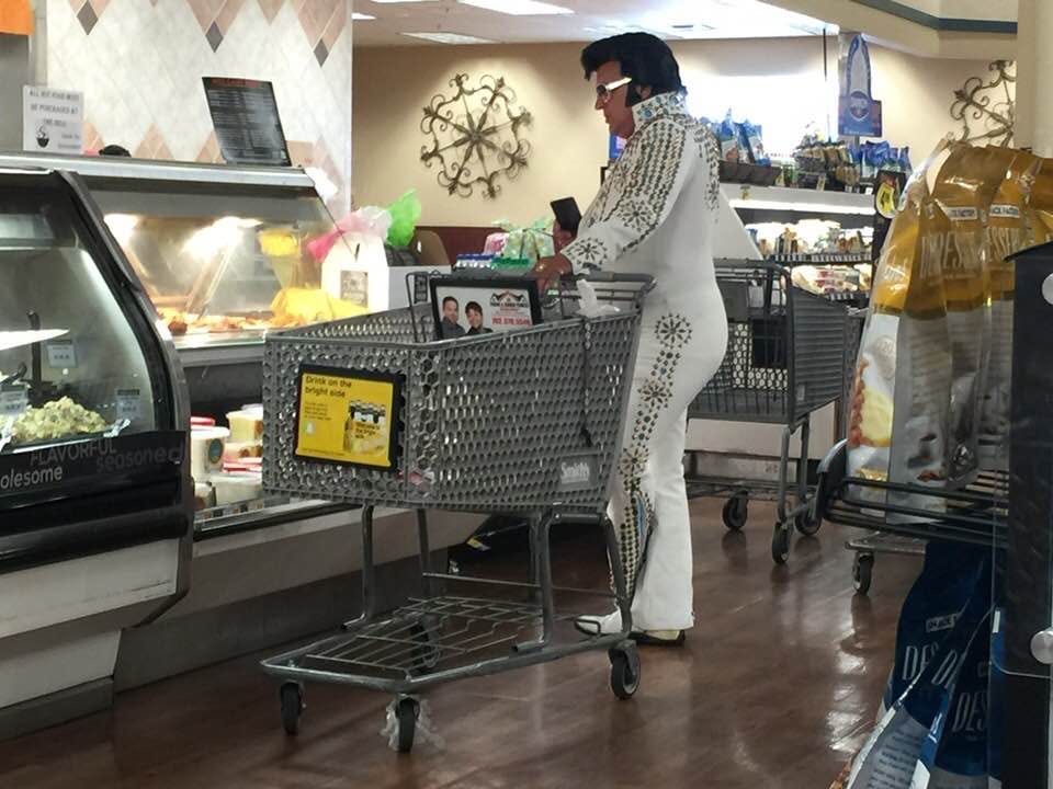 Ein Elvis-Presley-Imitator schiebt einen Einkaufswagen, während er in einem Lebensmittelgeschäft auf ein Regal mit Lebensmitteln blickt.