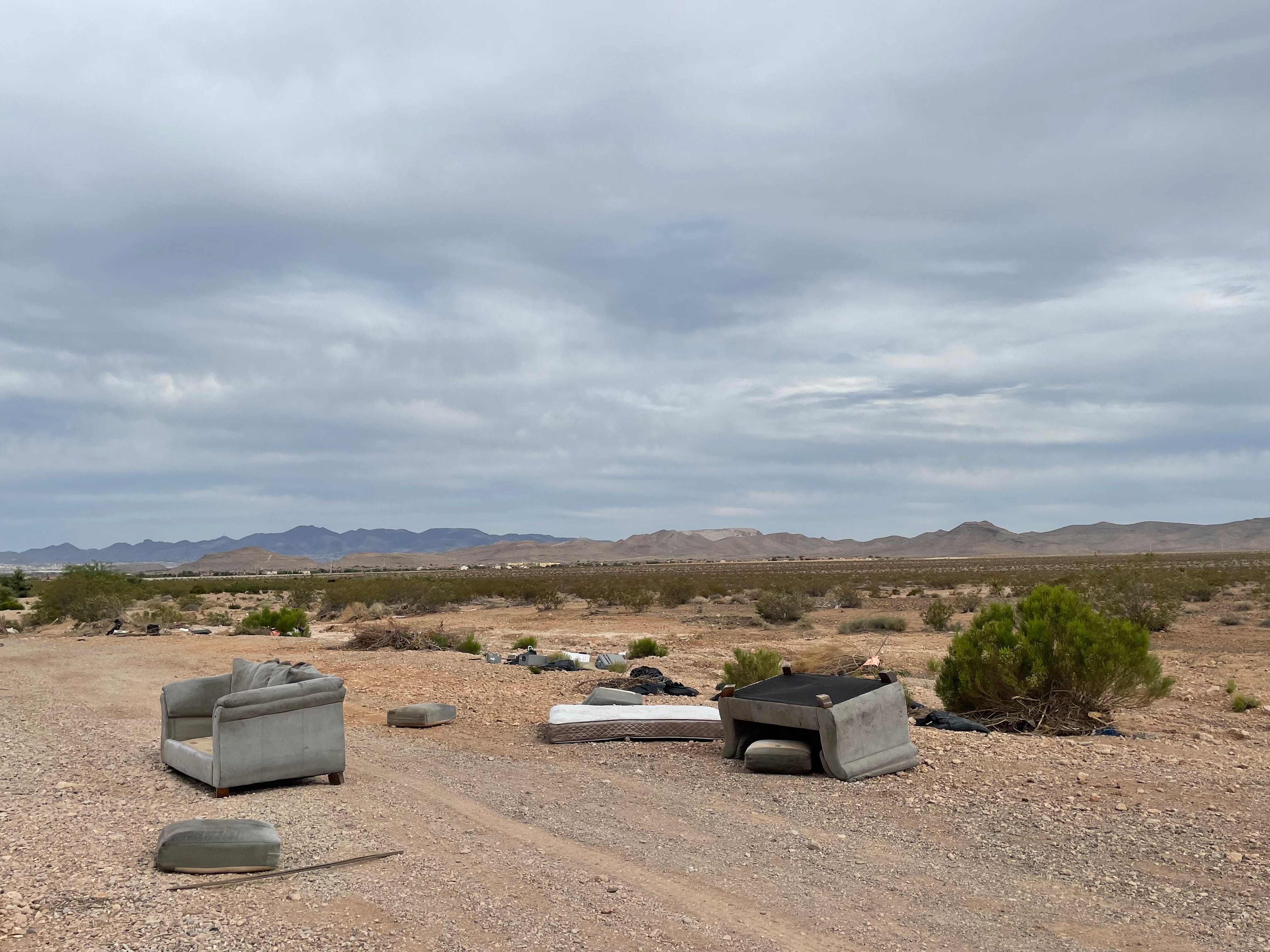 Zwei Sofas, eine Matratze und anderer Müll liegen am Rand einer unbefestigten Straße in der Wüste.