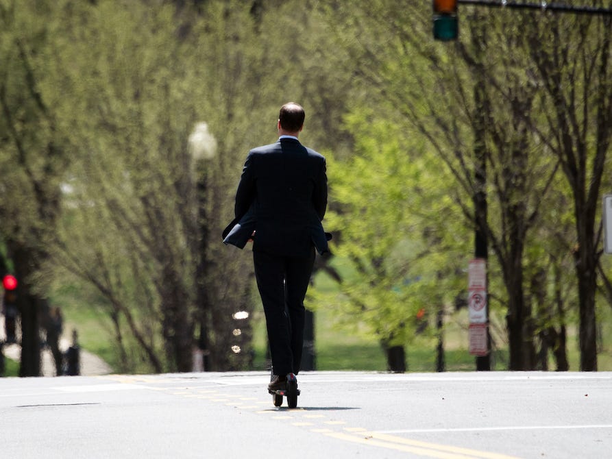Ein Mann im Anzug fährt mit seinem Elektroroller über eine Hauptstraße in Washington.