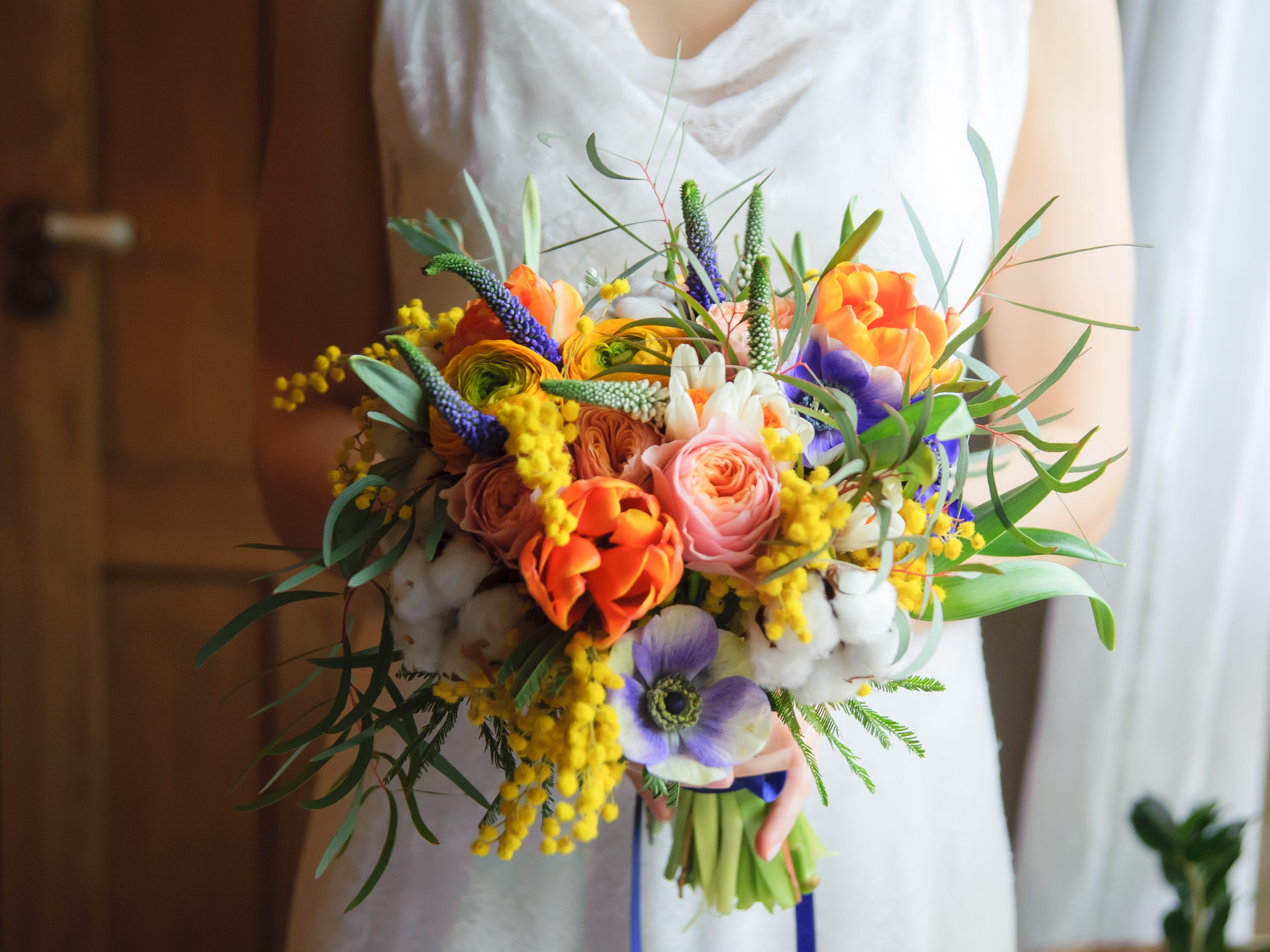 Eine Braut hält einen orangefarbenen, rosafarbenen und grünen Hochzeitsstrauß mit Blumen