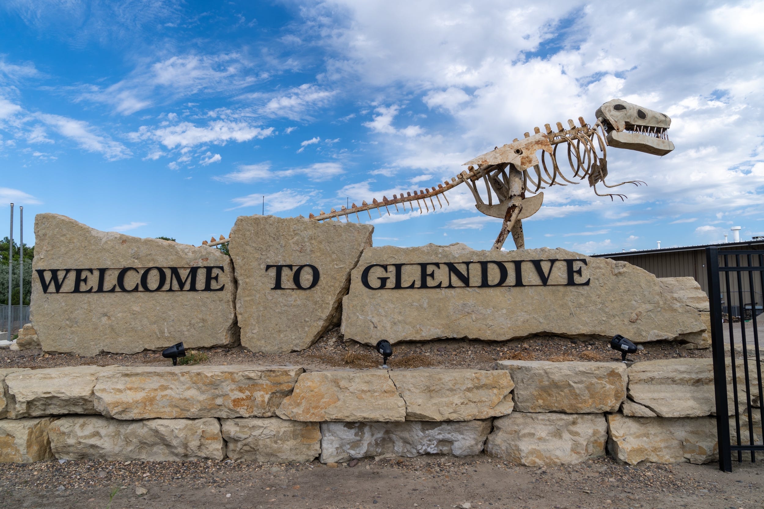 Ein „Willkommen in Glendive“-Schild mit einer Dinosaurierskelettstatue dahinter.
