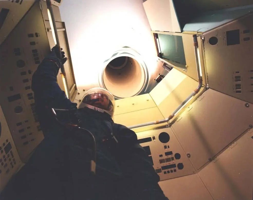 Ein Besatzungsmitglied im Anzug in einem Modell der MOL-Mannschaftskabine, das den engen Tunnel zeigt, der zur Gemini-B-Kapsel führt.