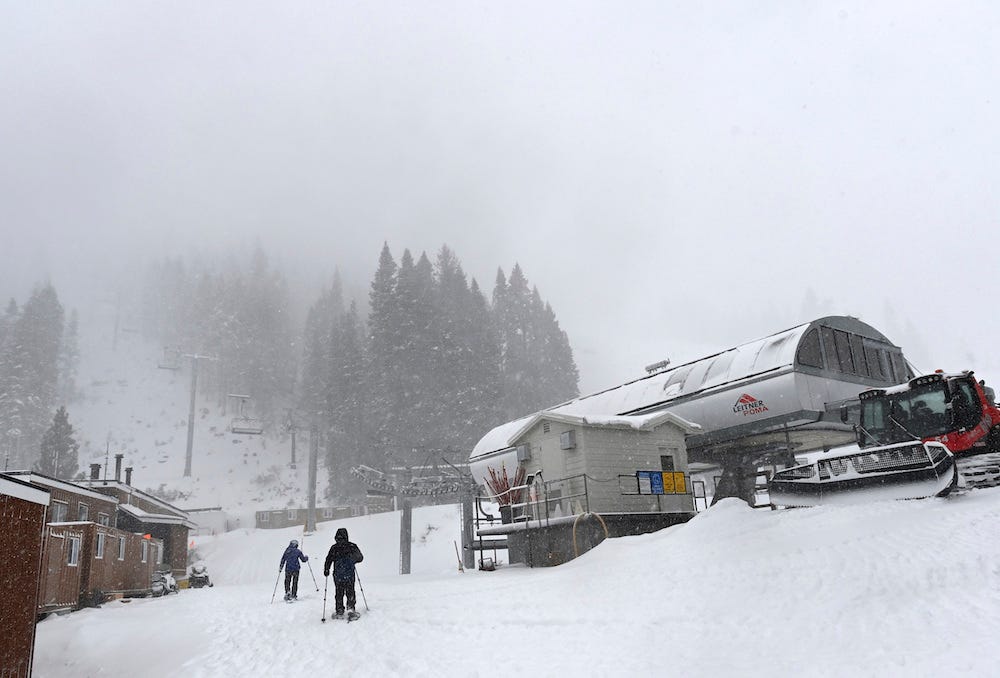 Menschen laufen am Mittwoch, den 10. Januar 2024, bei schwerem Wetter im Palisades Tahoe in Tahoe, Kalifornien, mit Schneeschuhen neben dem Skilift.
