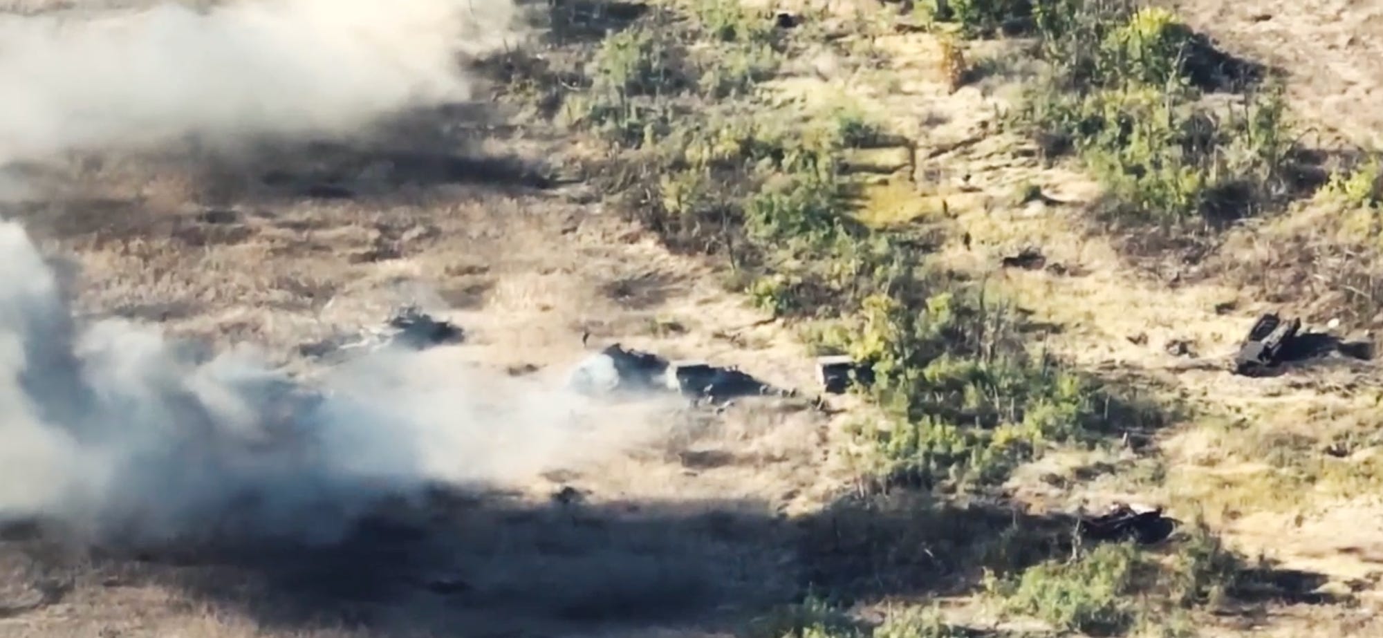 Ein Standbild aus Drohnenvideoaufnahmen zeigt rauchende Panzer auf einem braunen Feld.