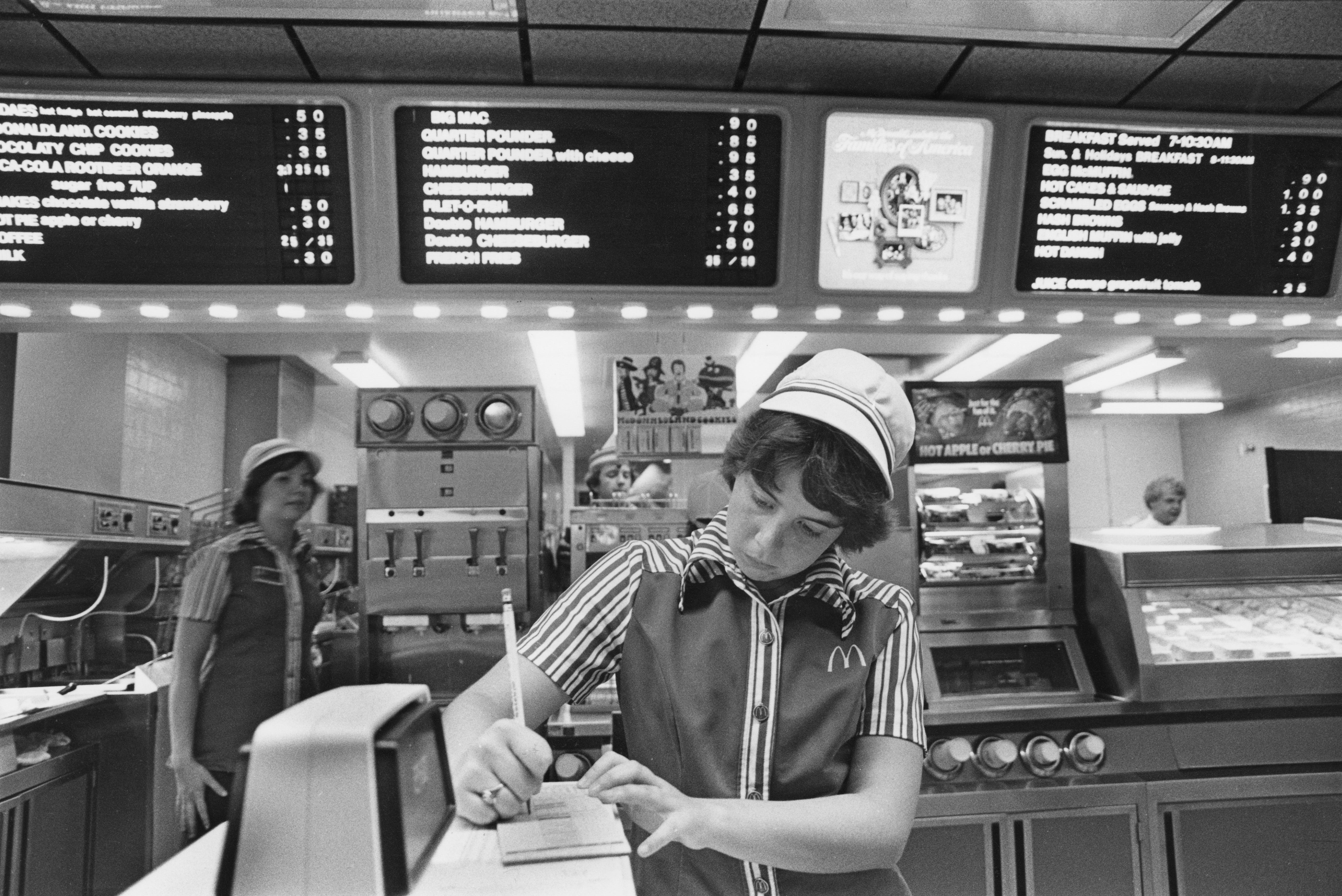 Ein Mitarbeiter macht sich Notizen an der Theke in McDonald's, Southfield, Michigan, USA, Juli 1978. Im Hintergrund sind Menütafeln zu sehen