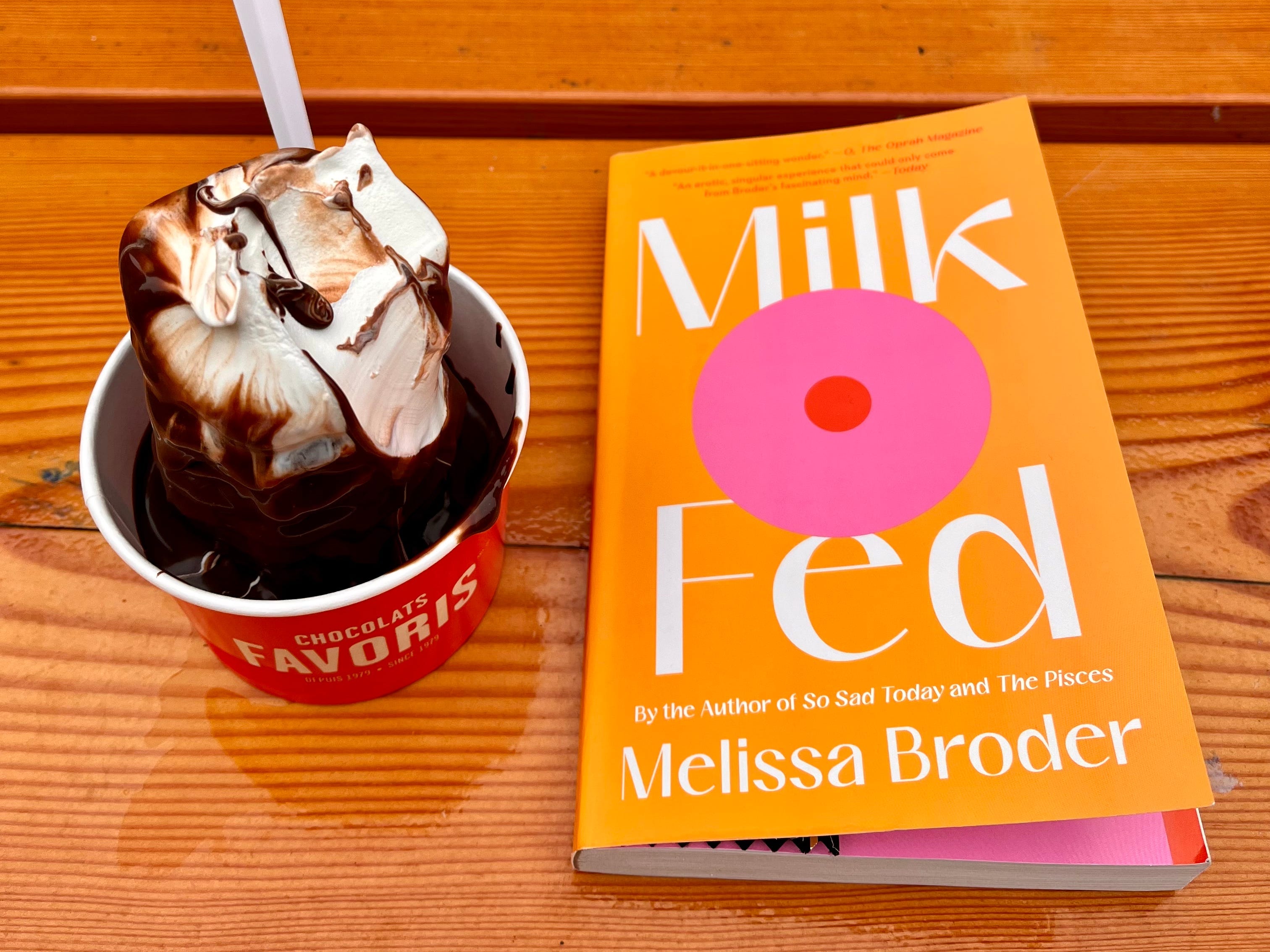 Eine Tasse Eis mit Schokoladensauce neben einem Exemplar des Romans „Milch gefüttert“ auf einem Tisch