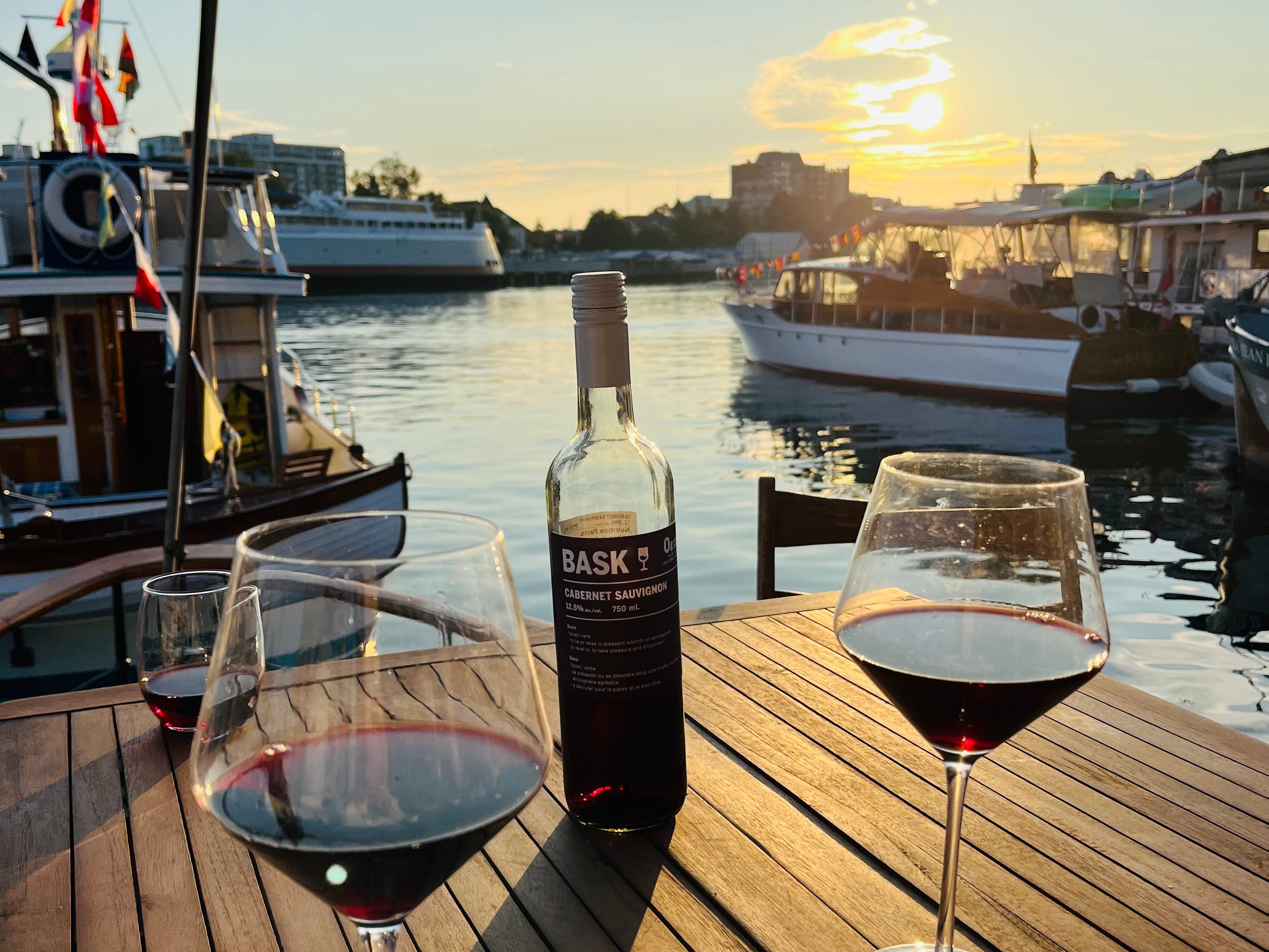 Gläser Wein um eine Flasche auf dem Deck eines Bootes mit Blick auf den Sonnenuntergang über dem Wasser